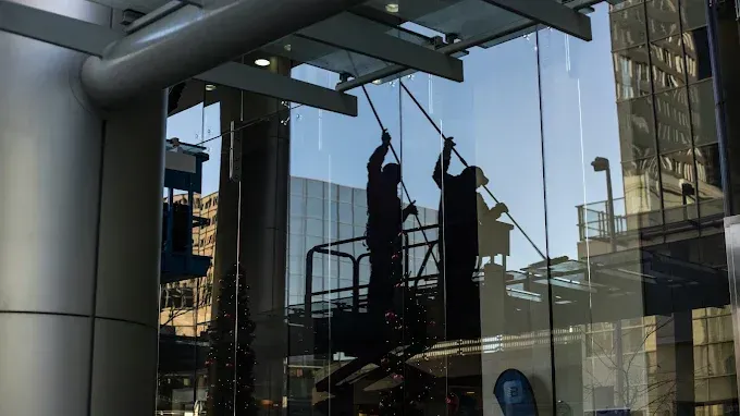 Two silhouetted workers hang from ropes outside a glass office building.