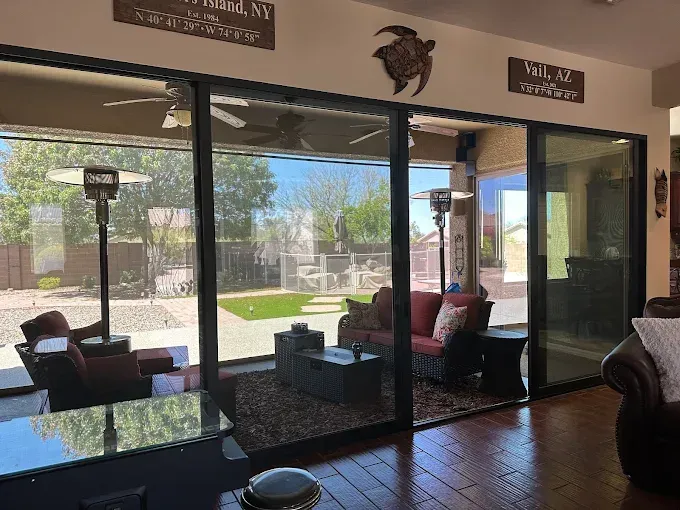 Patio living room with sliding glass doors, dark furniture, and a sunny backyard view