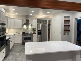 A modern kitchen with white cabinets, stainless steel appliances, a large marble island, and recessed shelving.