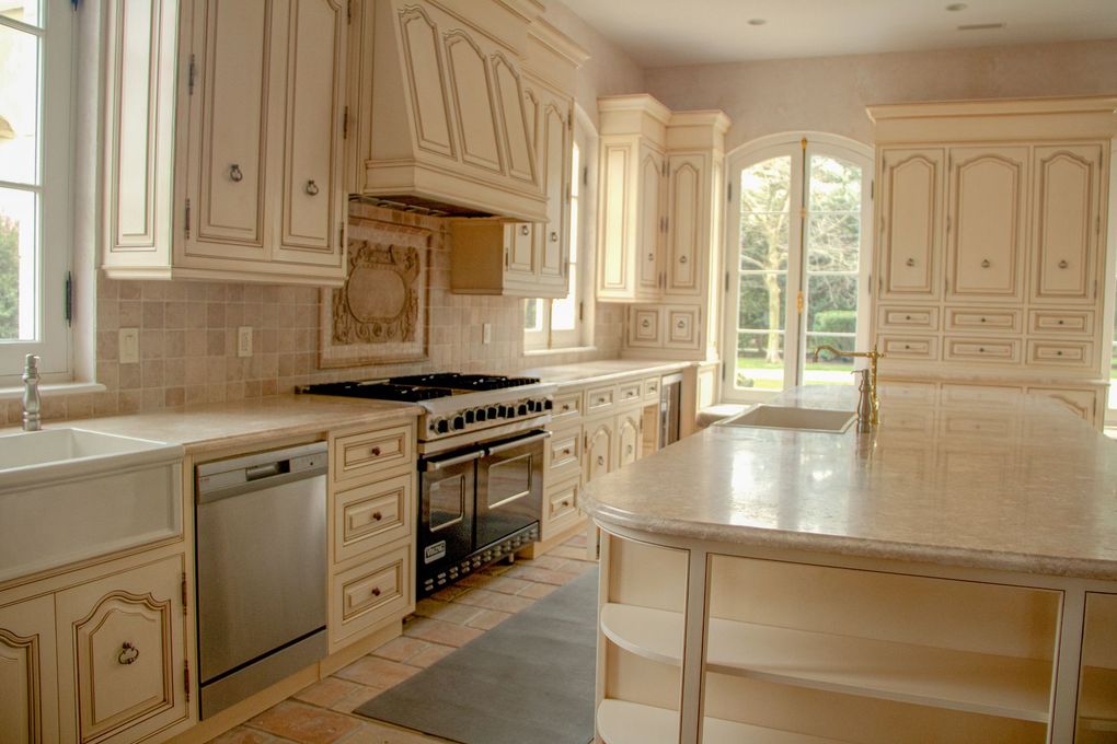 A spacious, bright kitchen featuring cream-colored distressed cabinets, a large island, and stainless steel appliances.