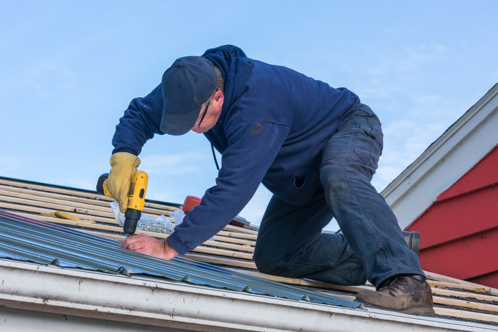 A professional roofer using a power drill to perform a roof leak repair on a metal rooftop.