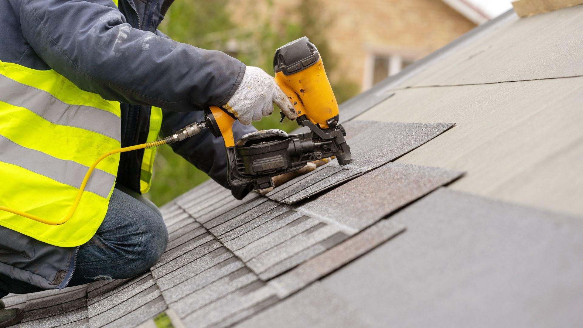 A close-up of a roofer using a pneumatic nail gun to install tiles on a roof.