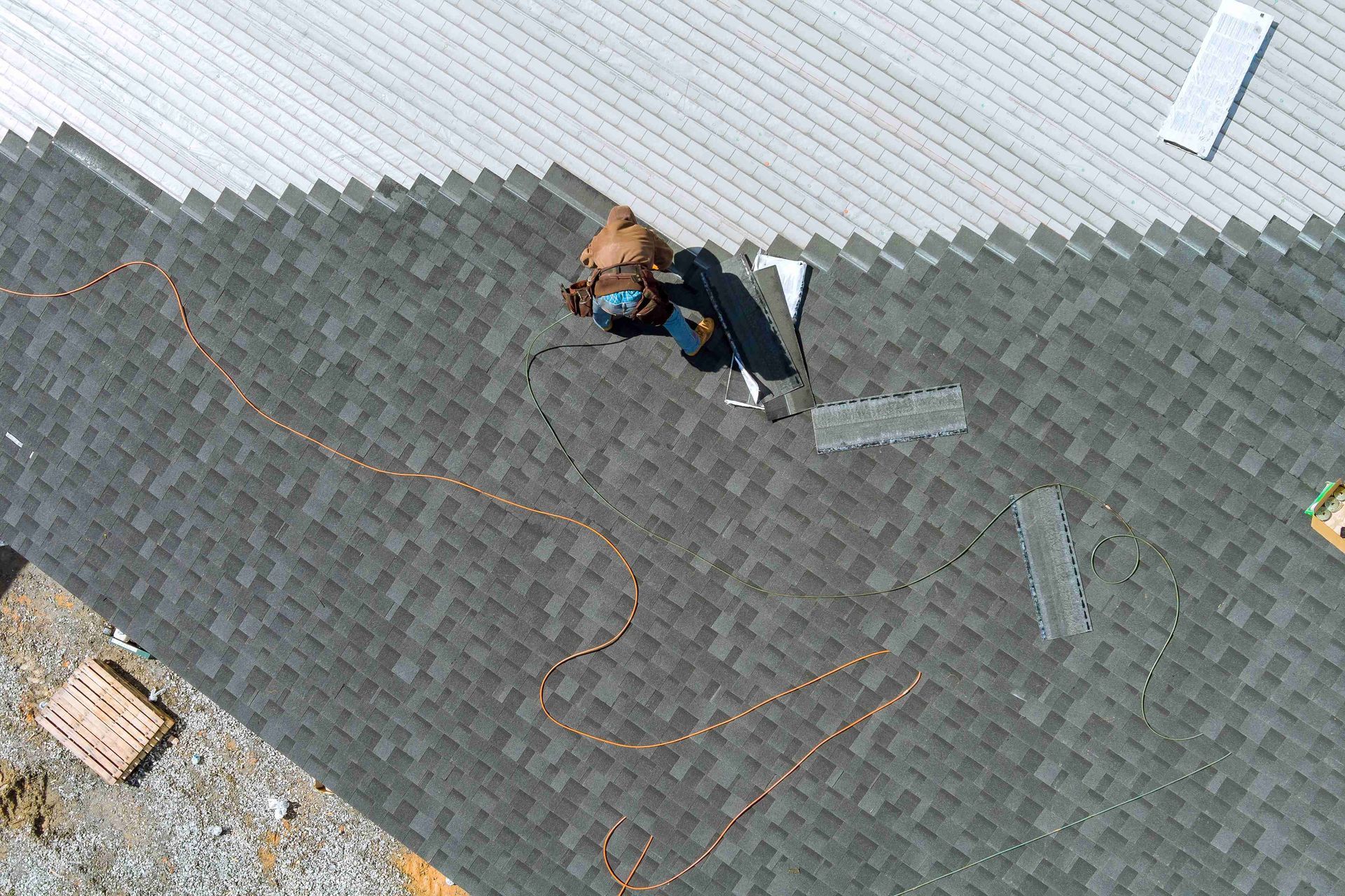 Roofer installs shingles on a residential roof with tools and safety lines. Roofer installs shingles on a residential roof with tools and safety lines.