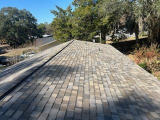 View of an asphalt shingle roof, varying shades of gray, under a sunny sky.