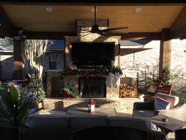 Cozy patio with a mounted TV above a stone fireplace, potted plants, and cushioned outdoor seating