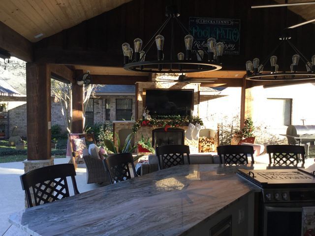 Covered outdoor patio with wooden table, black chairs, and a fireplace in the background