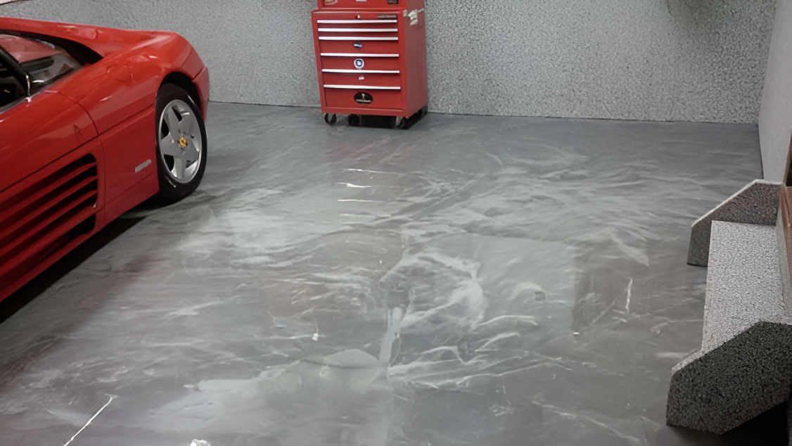 Red sports car in a garage beside a red tool chest on a gray concrete floor.