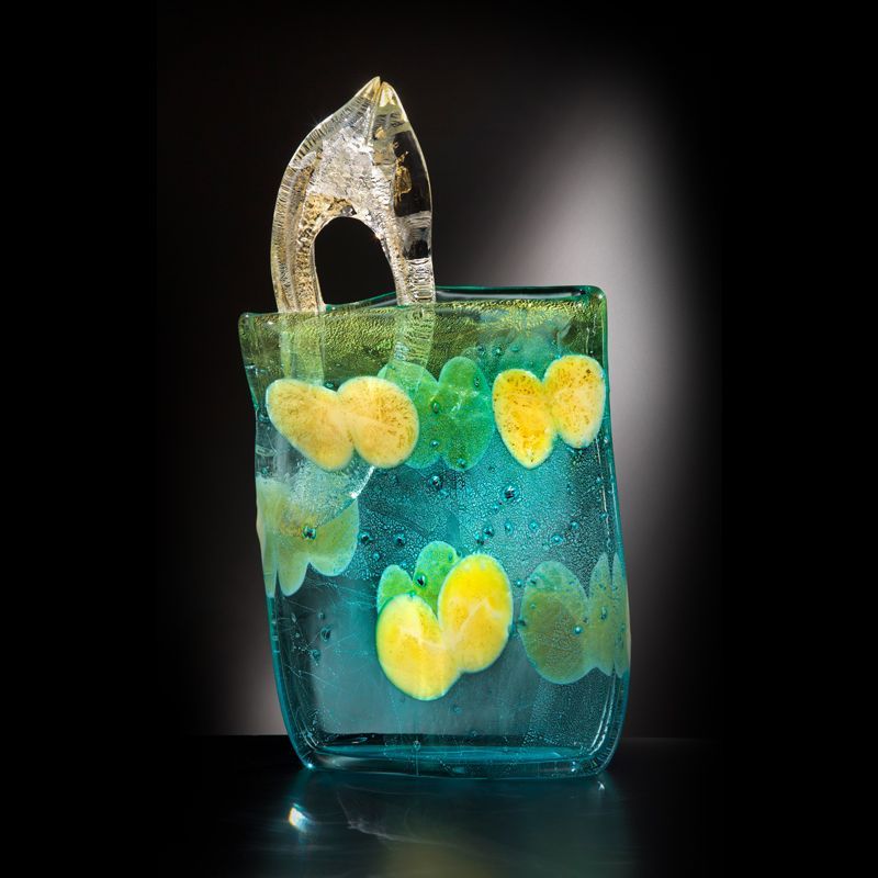 Turquoise glass vase with yellow and green floral designs, clear handle, against a black background.