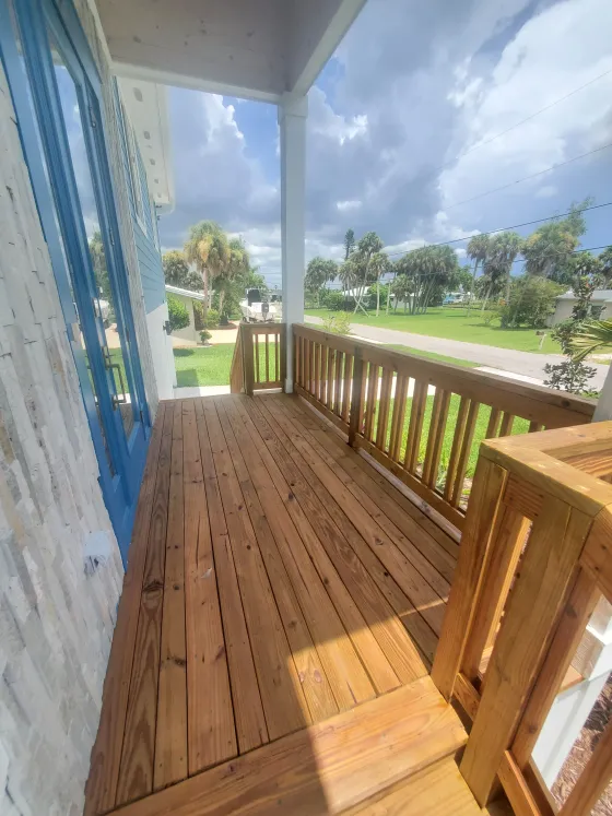 Wooden front porch with railing, blue curtains, and a view of green lawn under cloudy sky.