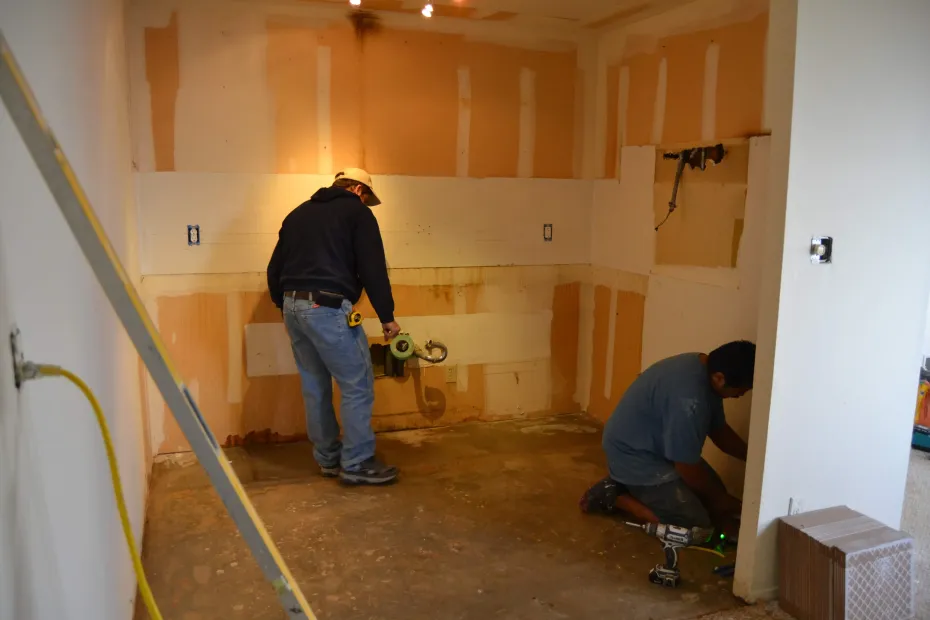 Two workers sanding and repairing drywall in a room under renovation