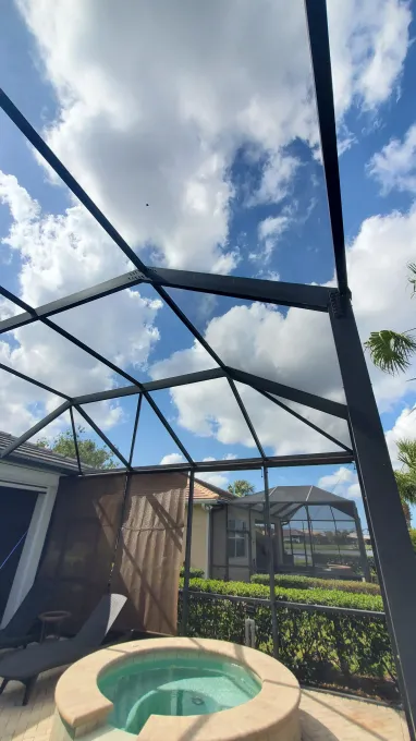 Patio with screened enclosure, hot tub, lounge chair, and cloudy sky overhead
