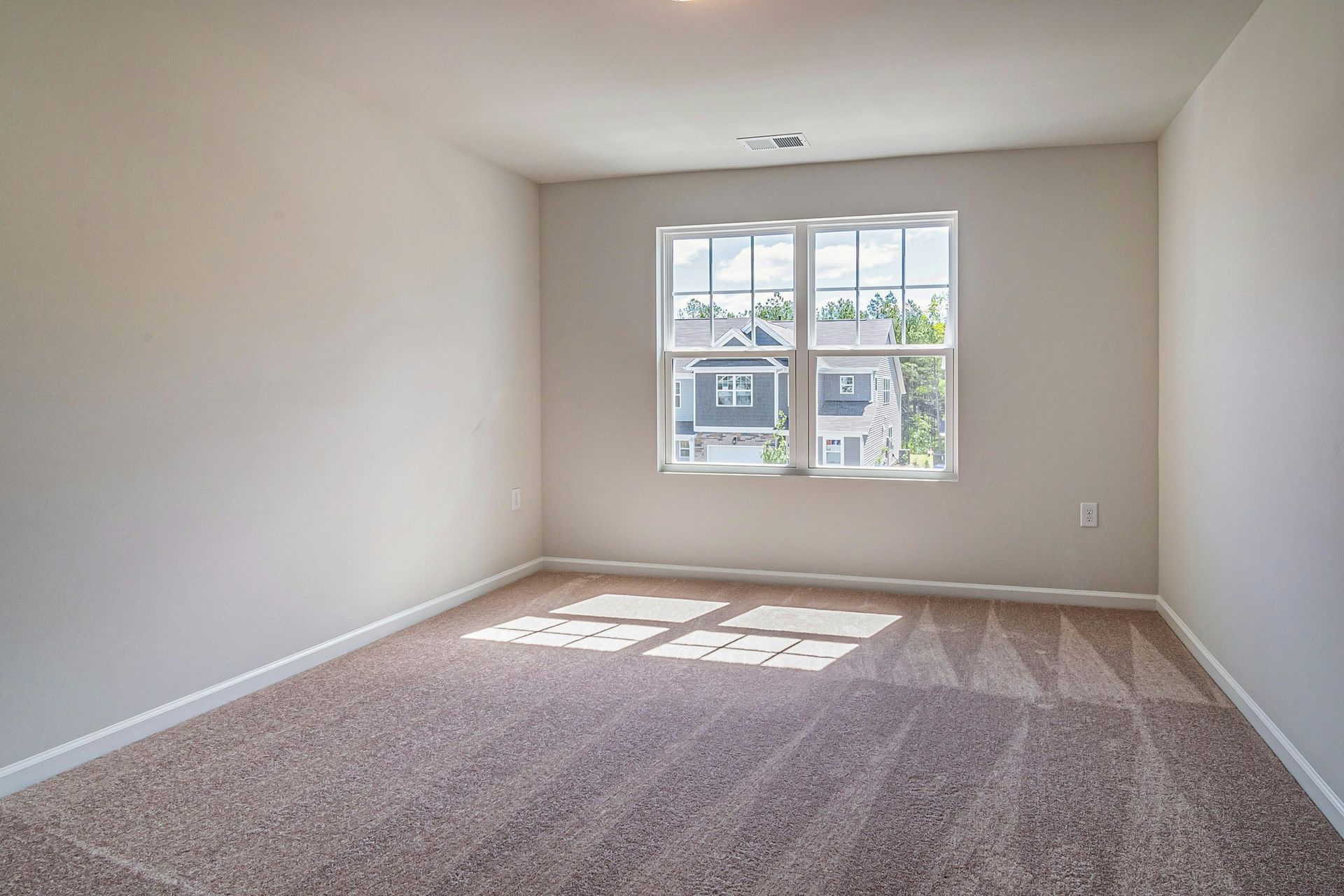 Empty beige carpeted bedroom with a window letting in sunlight