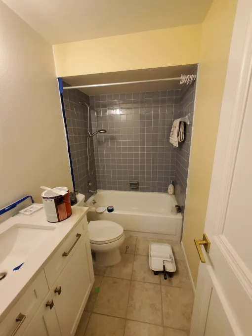 Small bathroom with a white toilet, vanity, and tiled tub-shower alcove in gray.