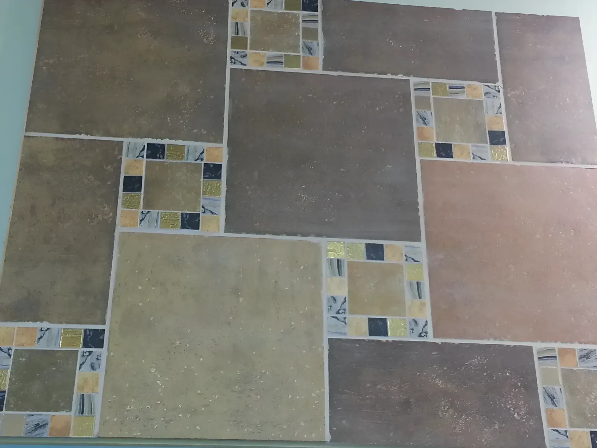Patterned ceramic floor tiles in beige, brown, and gray squares with mosaic accents