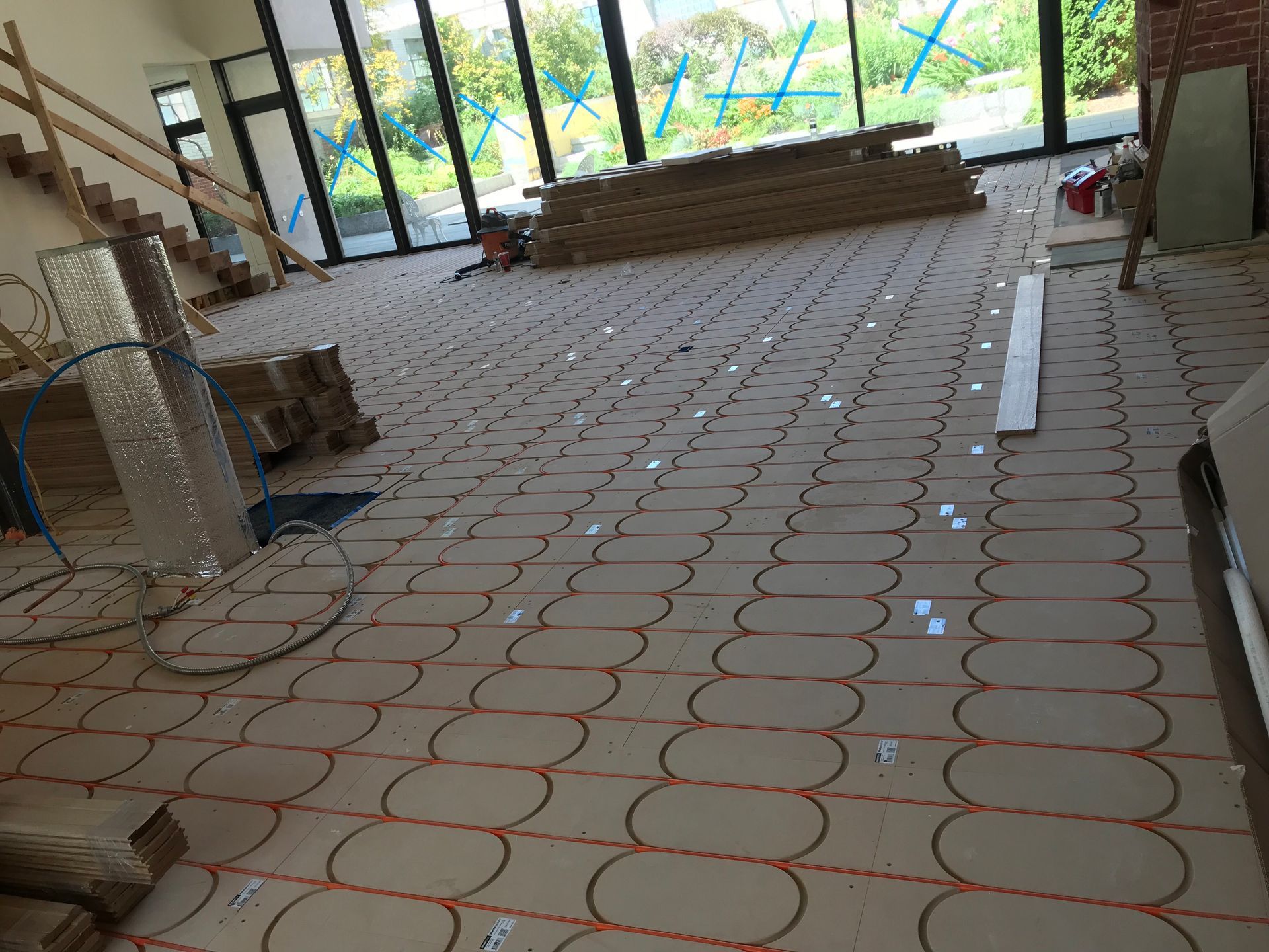 Construction site with tiled floor, stacked materials, and large windows letting in daylight.