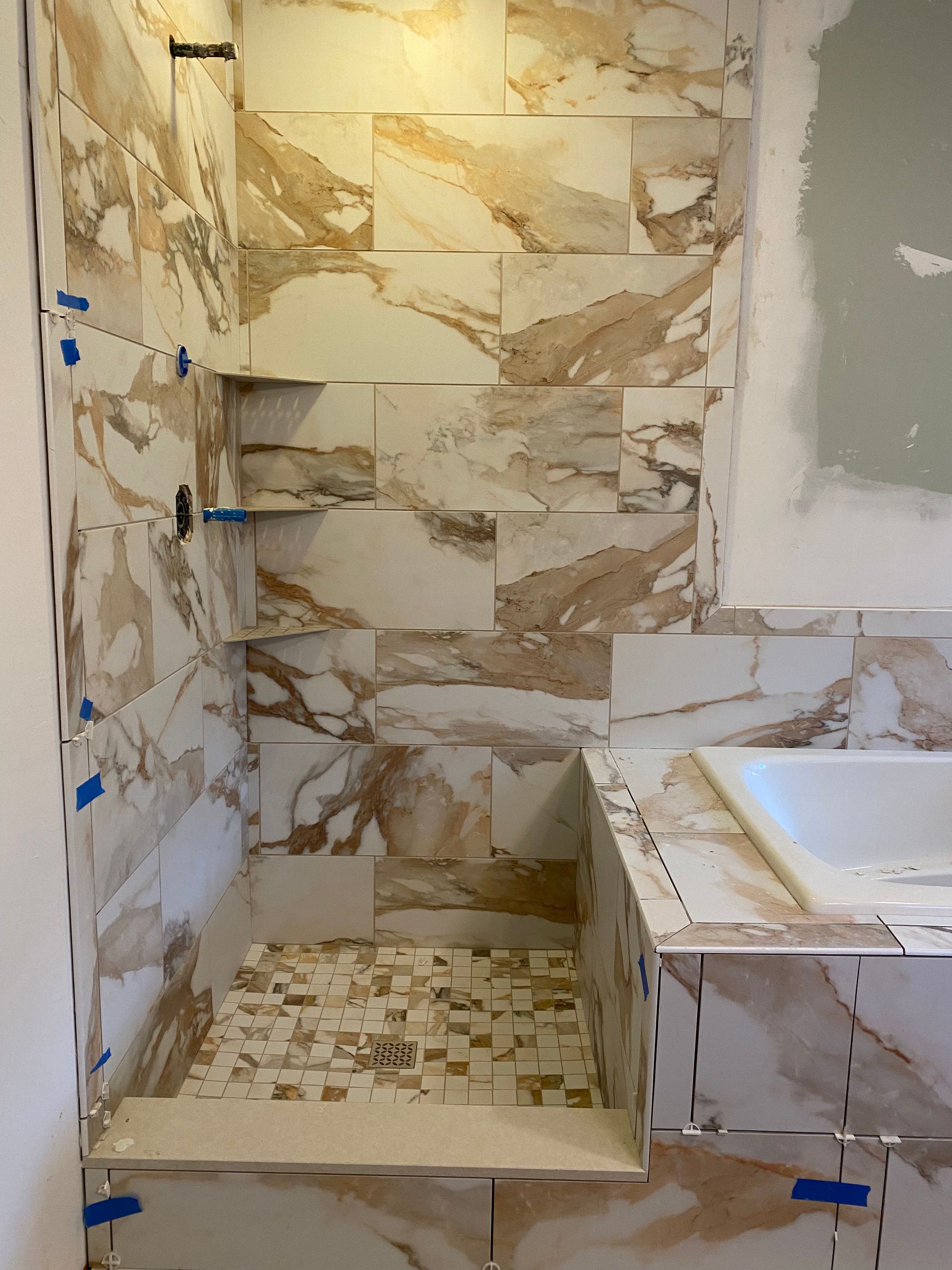 Partially tiled bathroom shower with beige stone-pattern tiles and a white bathtub edge