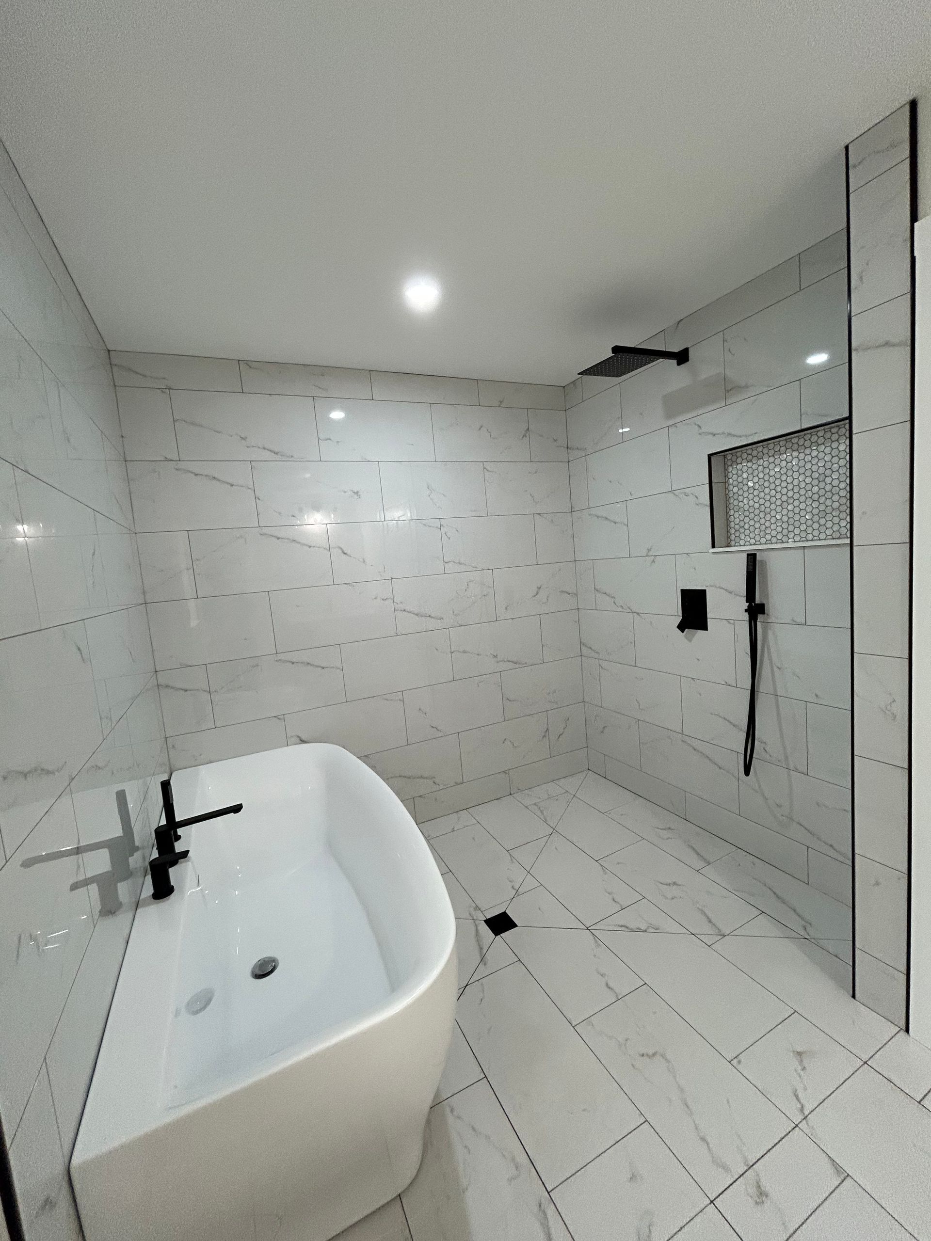 Modern white bathroom with a freestanding tub, wall tiles, glass shower, and ceiling light