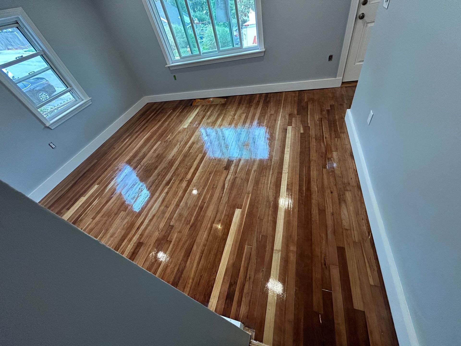 Empty room with glossy hardwood floor, gray walls, and windows letting in daylight