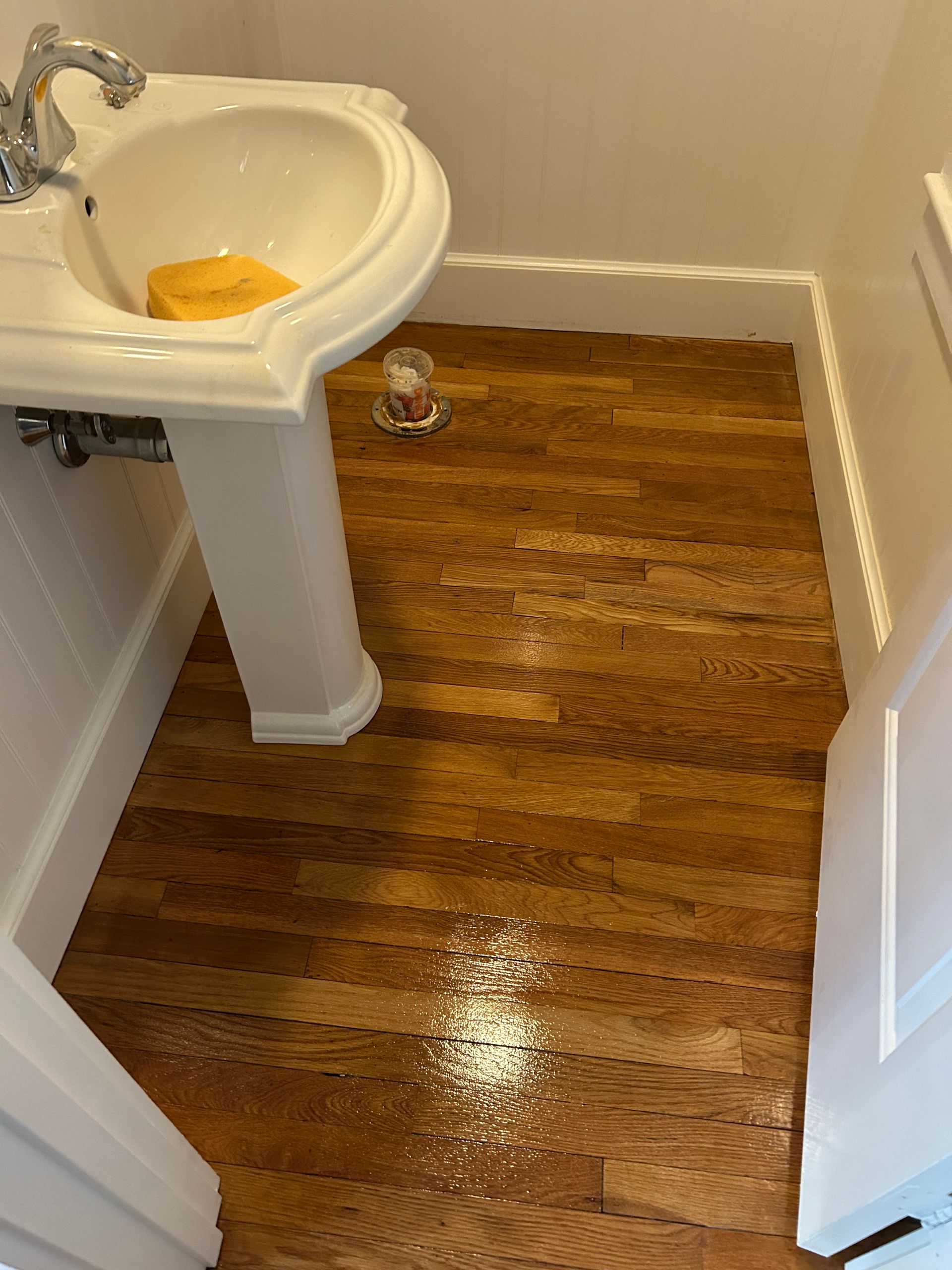 Small bathroom with a white pedestal sink and wet hardwood floor.