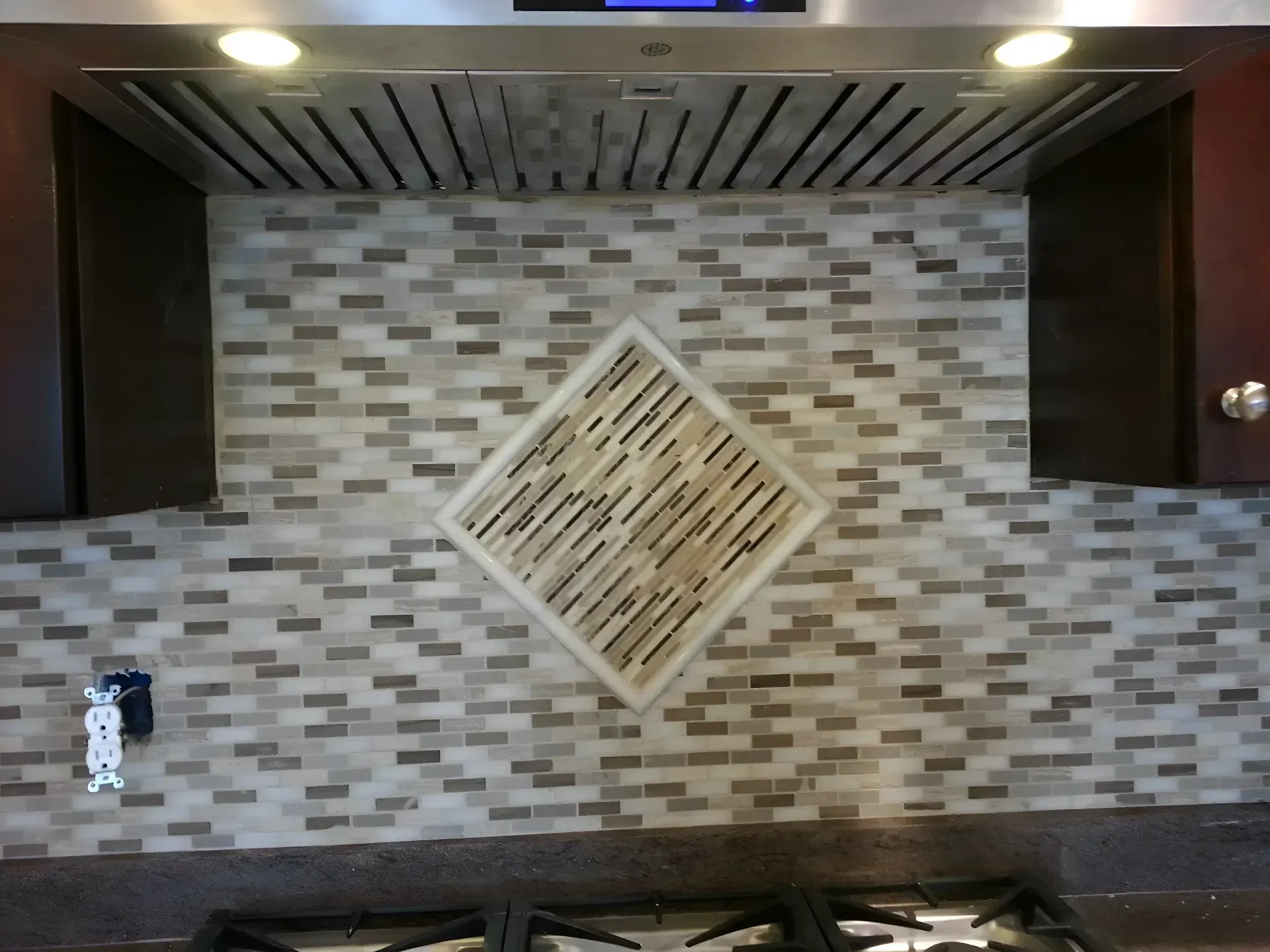 Kitchen backsplash with beige mosaic tiles and a diamond accent beneath a vent hood