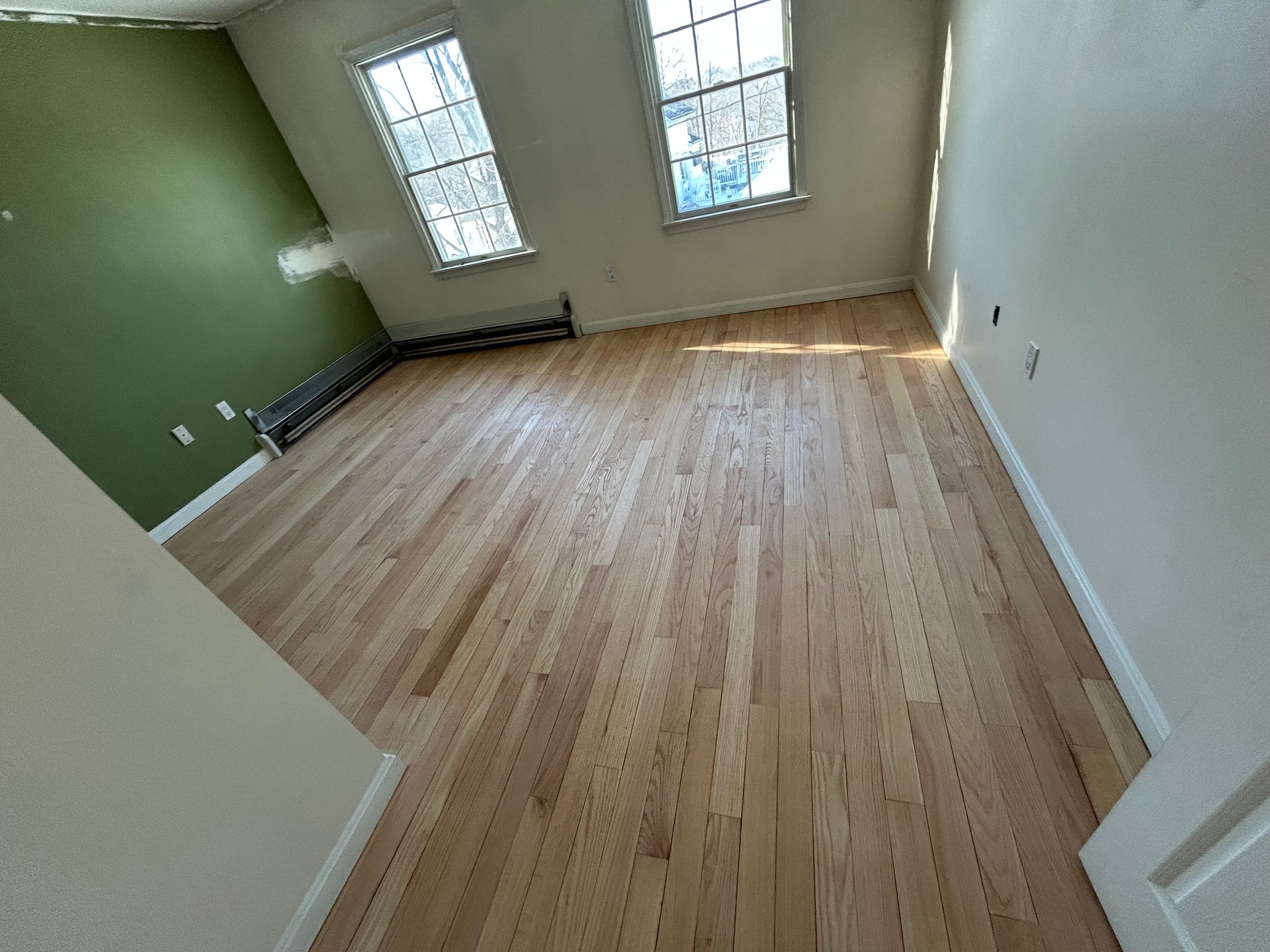 Empty hardwood-floored room with white walls and sliding glass doors leading to a bright outdoor patio.