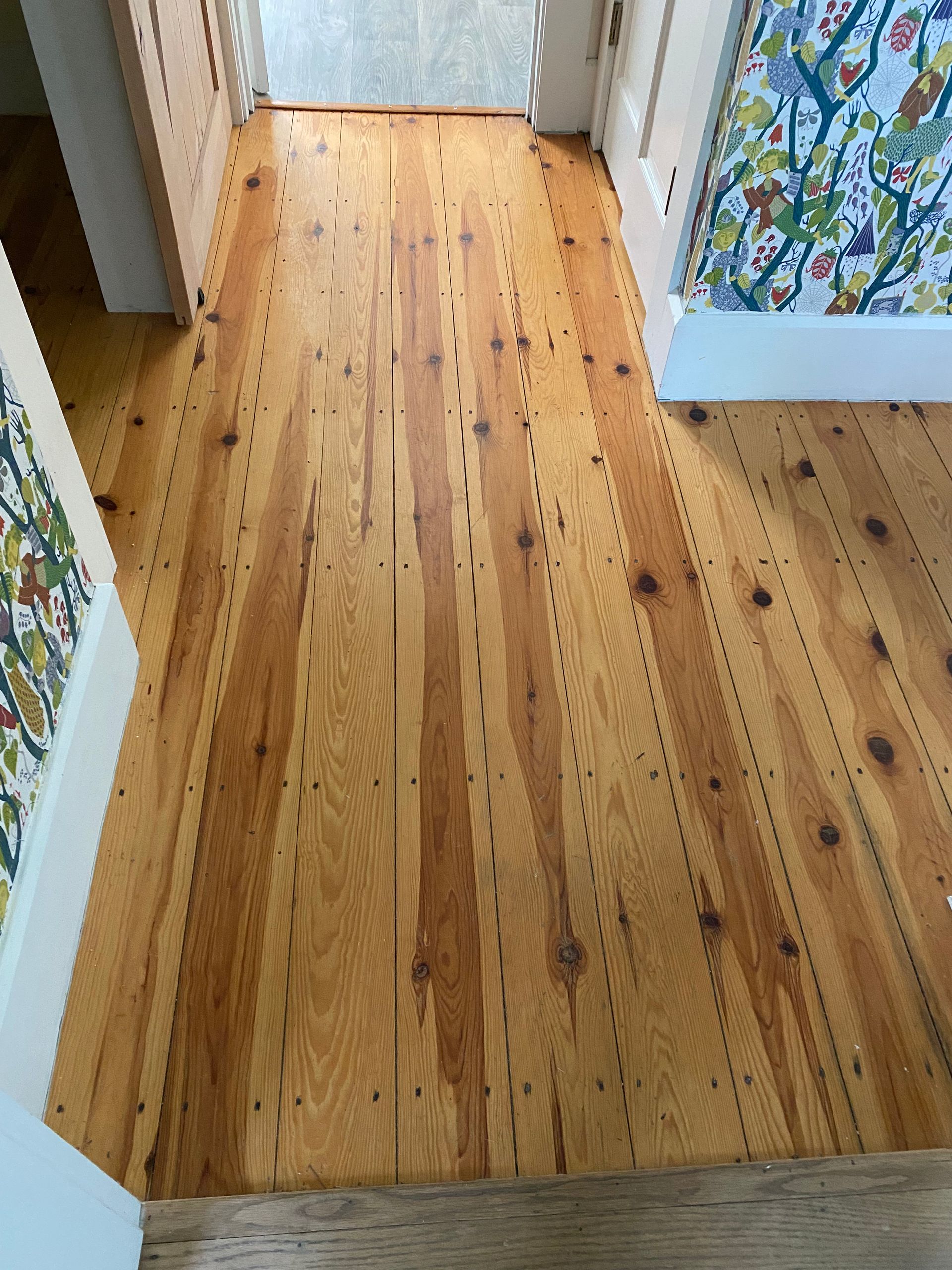 Narrow wooden hallway floor with visible knots and a colorful floral cabinet at the right edge
