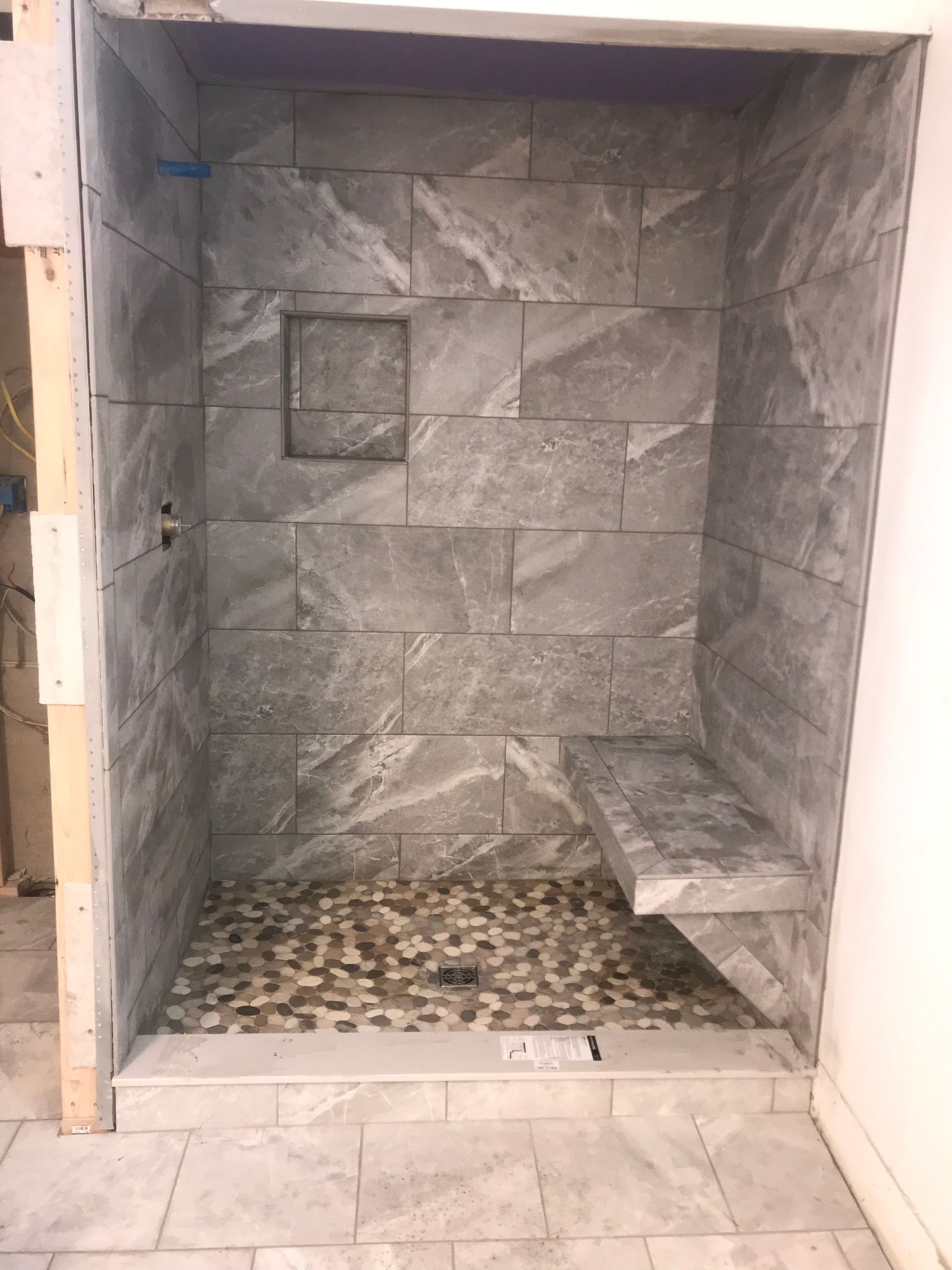 Empty tiled shower stall with gray stone walls and pebble floor in a bathroom
