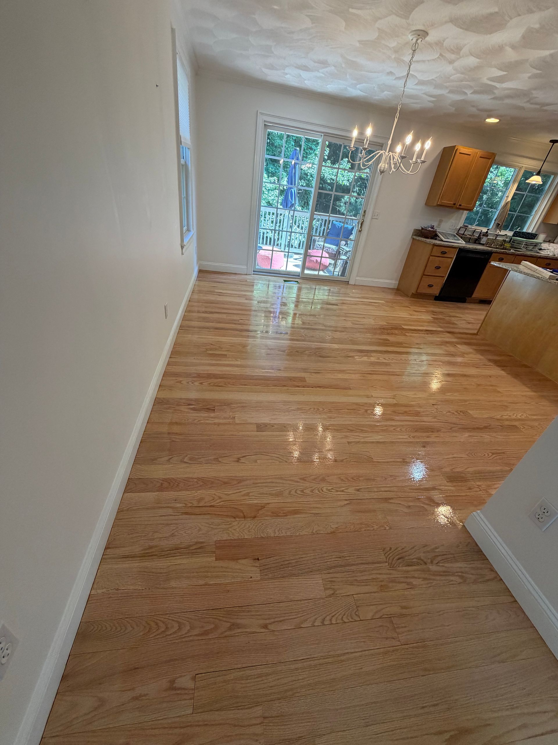 Empty sunlit living room with polished wood floors, white walls, and sliding glass doors to a patio.