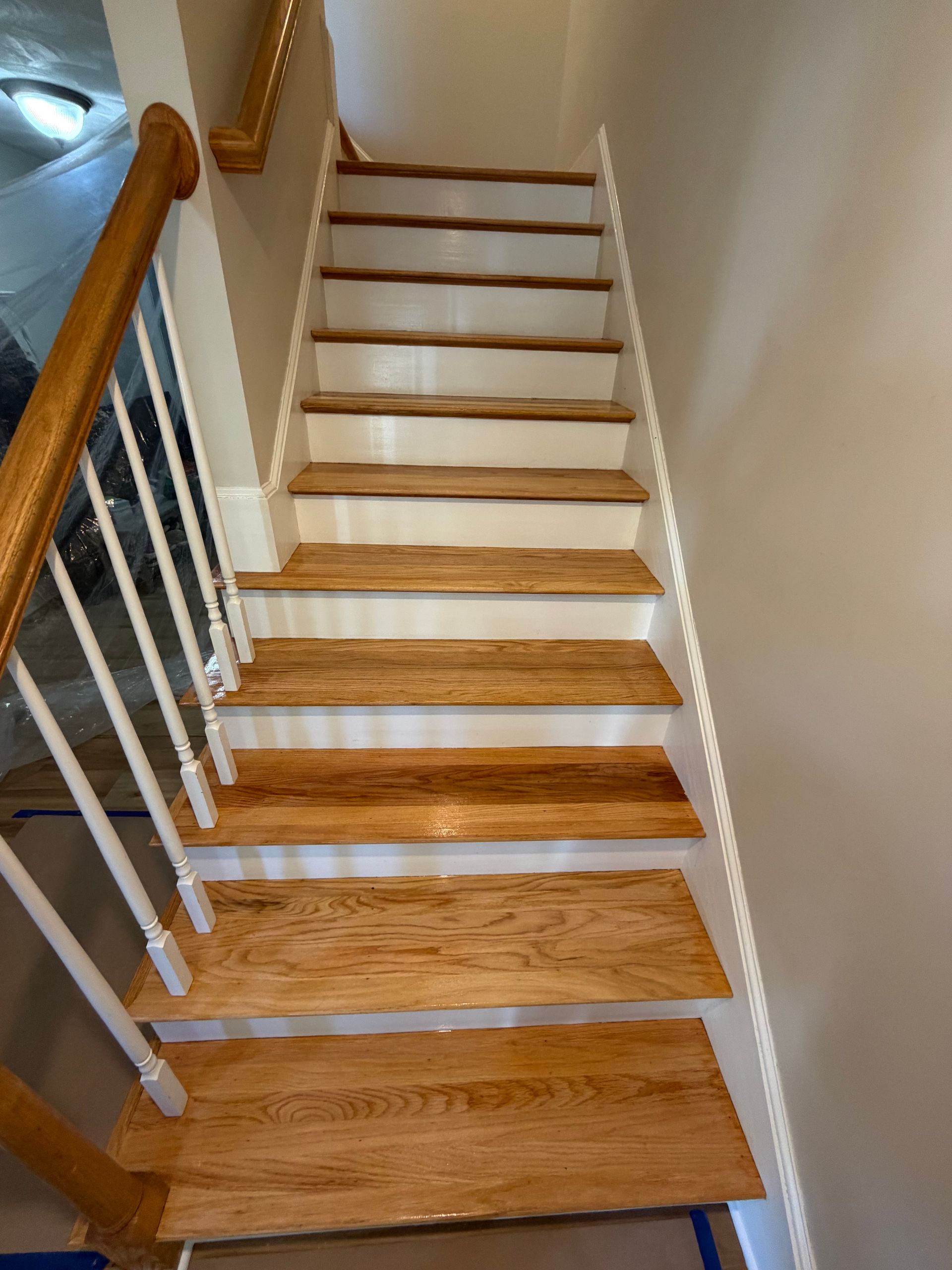 Narrow indoor staircase with wooden steps, white railings, and beige walls