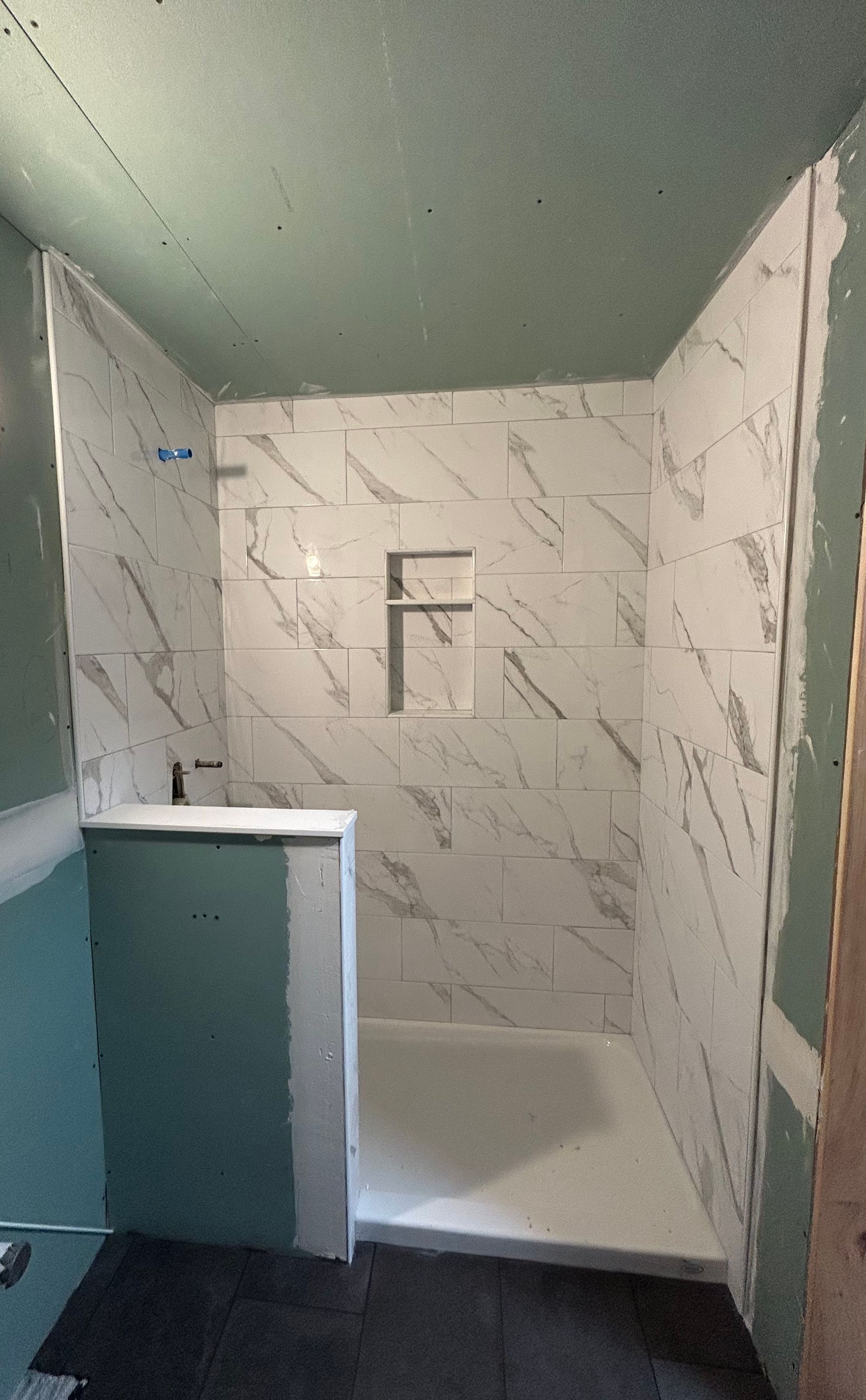 Small tiled shower stall with a half wall, glass side panel, and green ceiling.