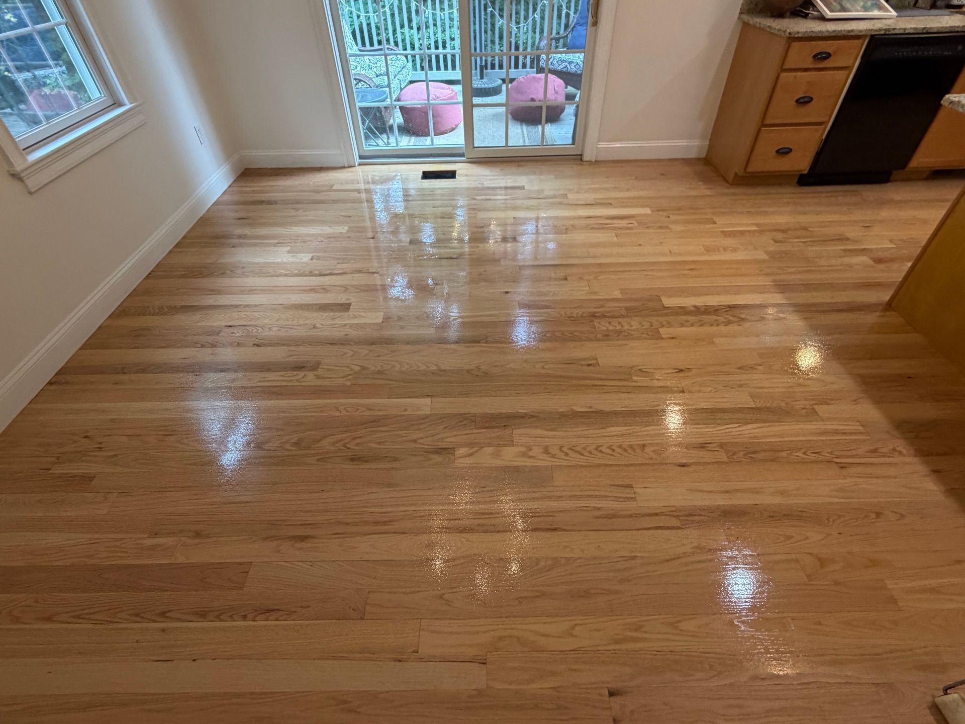 Empty hardwood living room with sunlight reflecting on the floor and sliding glass doors at the back.