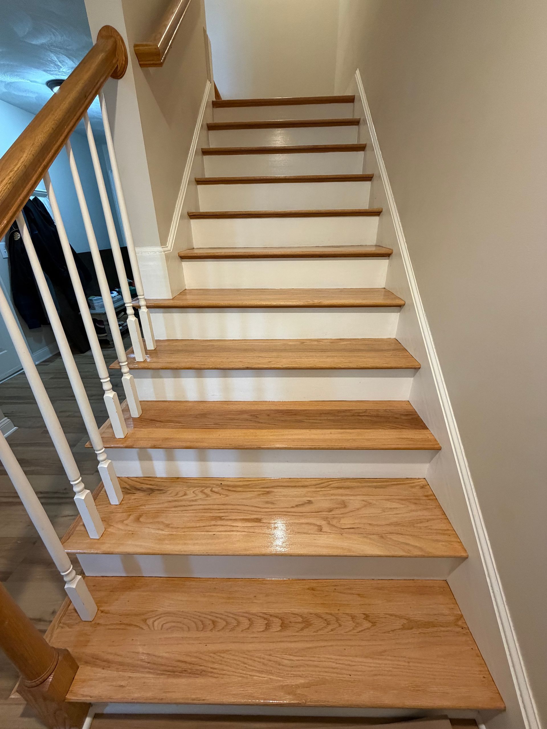 Indoor wooden staircase with white balusters and beige walls, viewed from the bottom upward