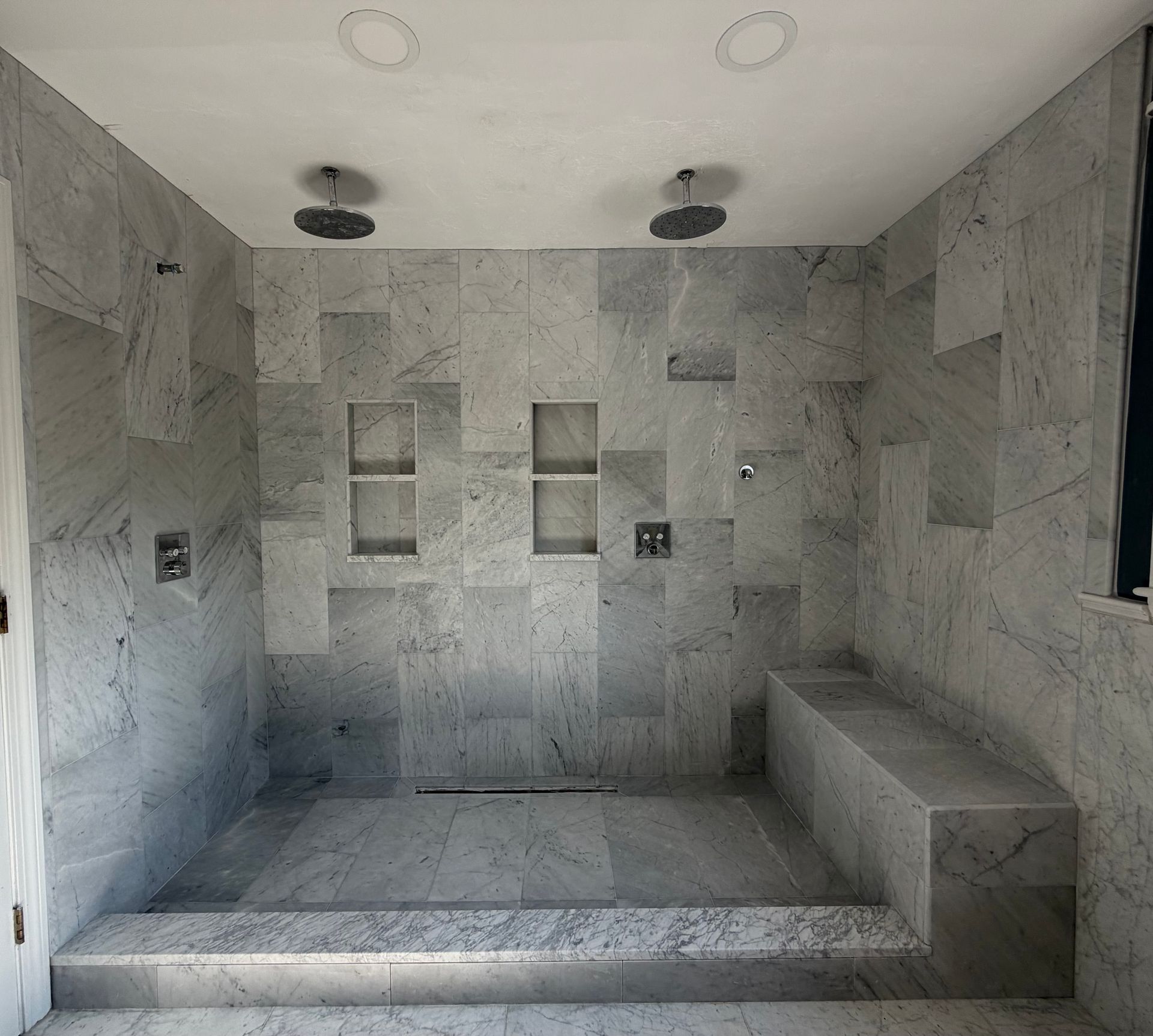 Stone shower room with built-in bench, recessed shelves, and overhead lights