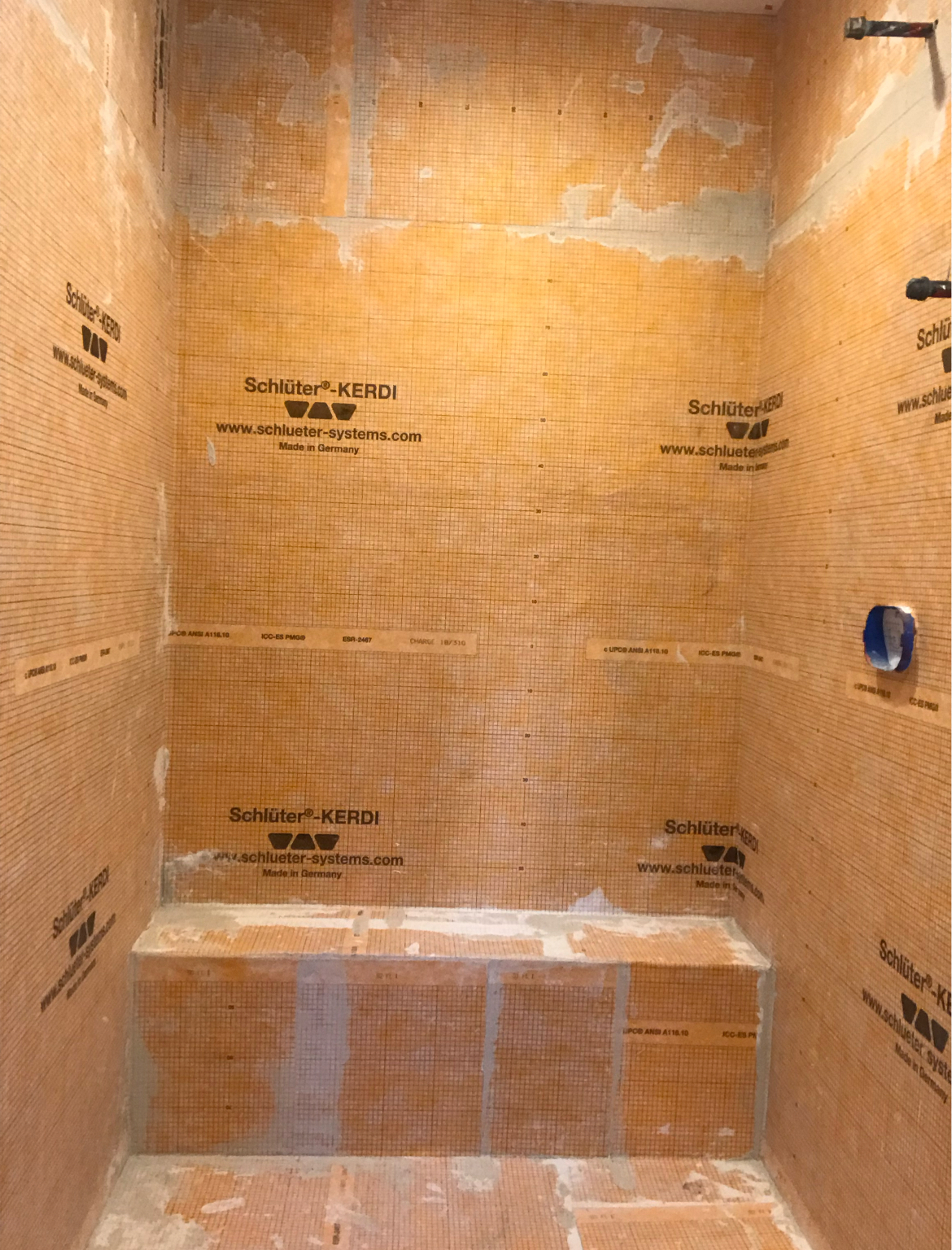 Unfinished tiled shower stall with tan waterproof membrane and built-in bench seat