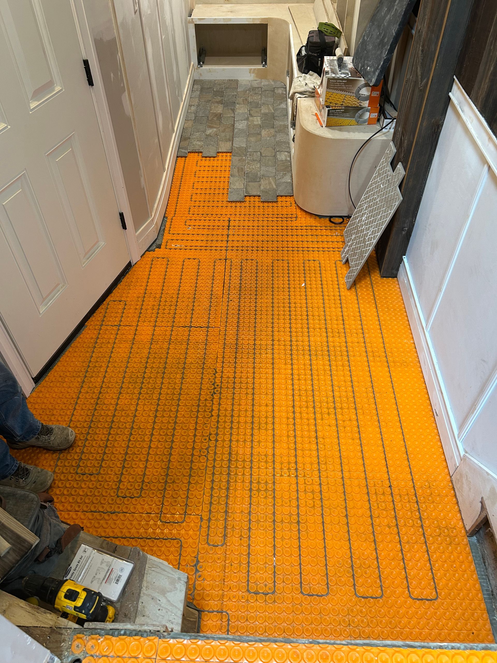 Orange underlayment with heating cable laid on a hallway floor during renovation.