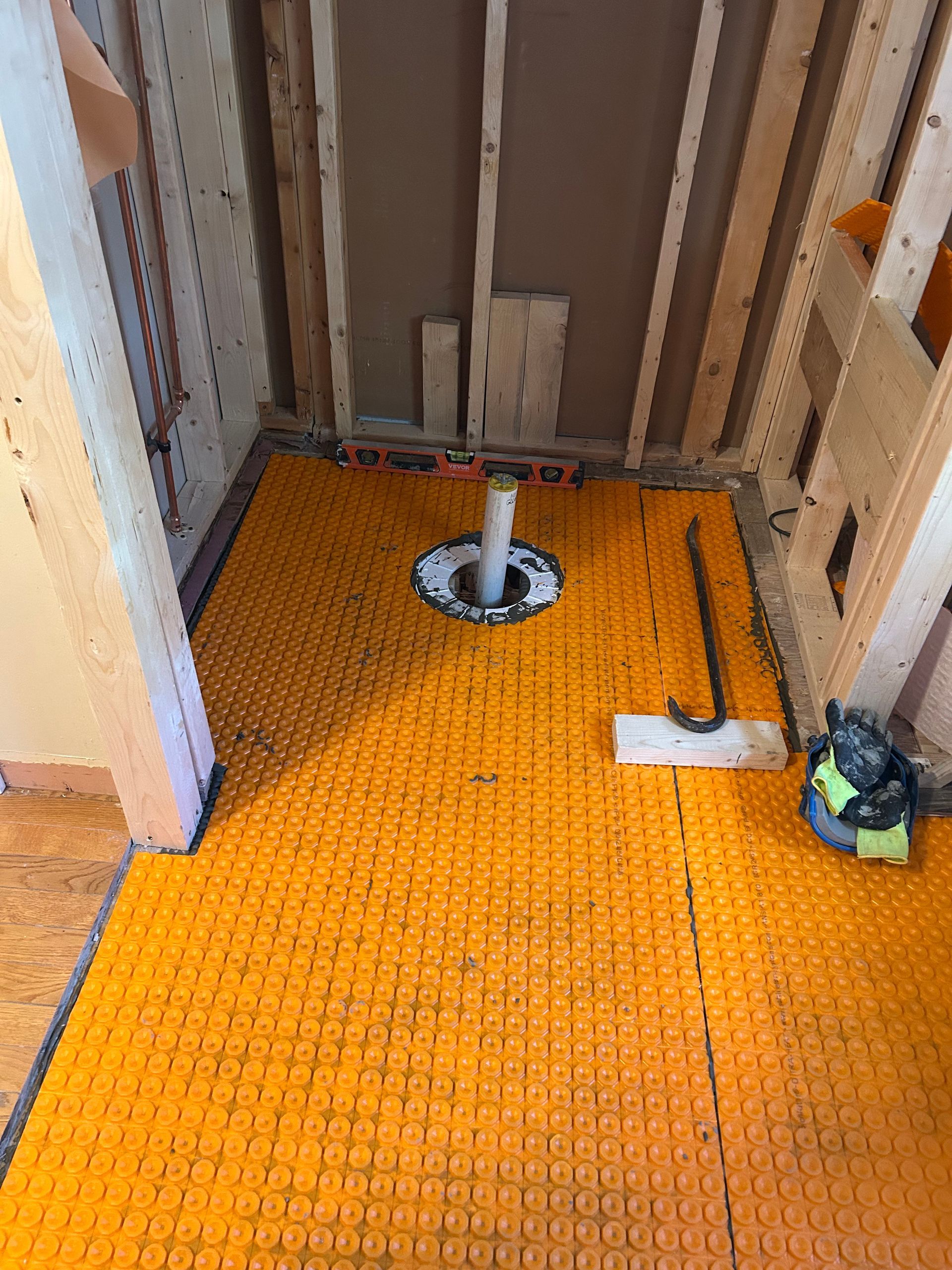 Small unfinished room with bright orange floor covering, exposed studs, and a central floor stand.