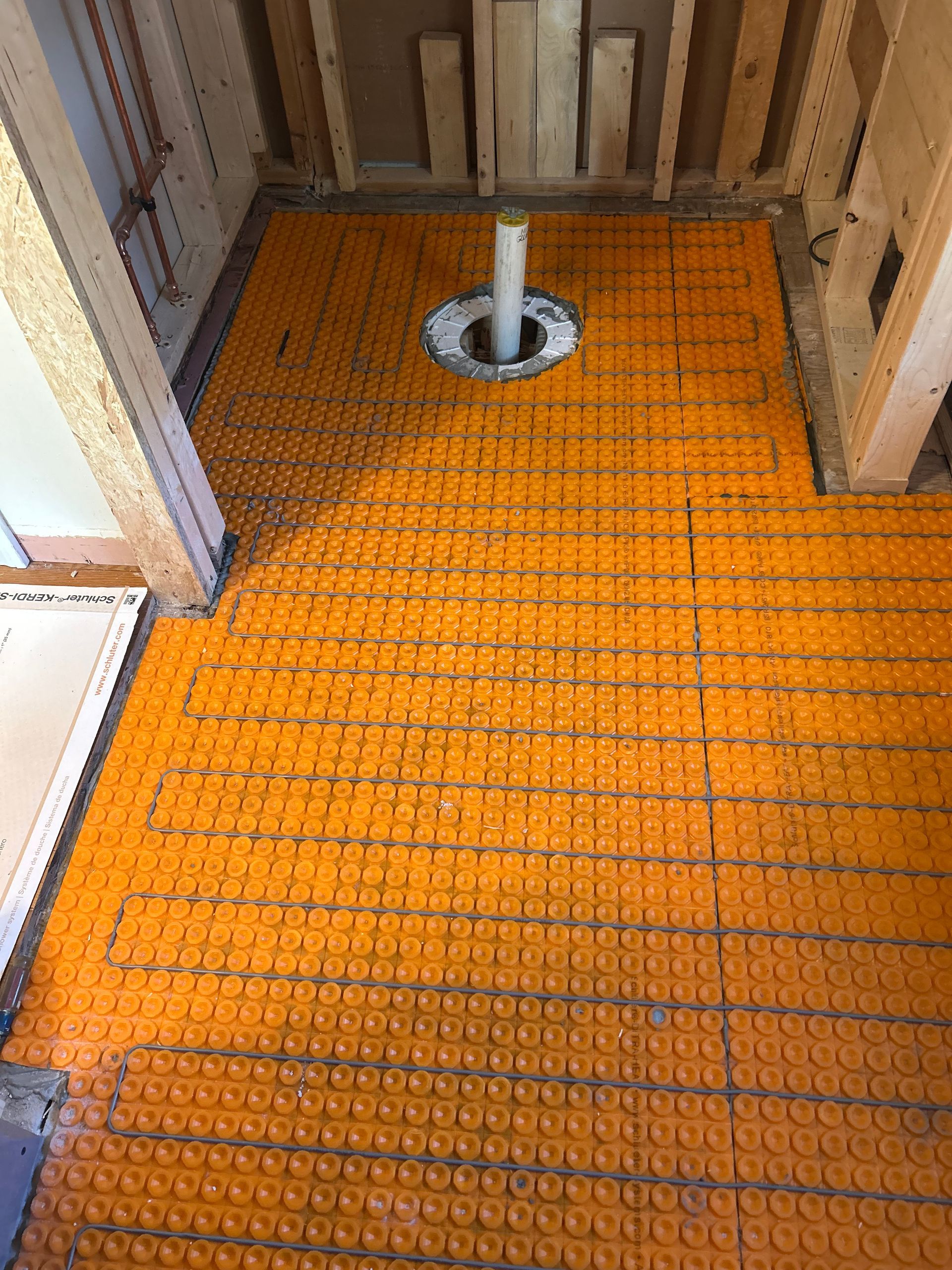 Orange mesh flooring inside a room, with a central metal pipe opening near the back wall.