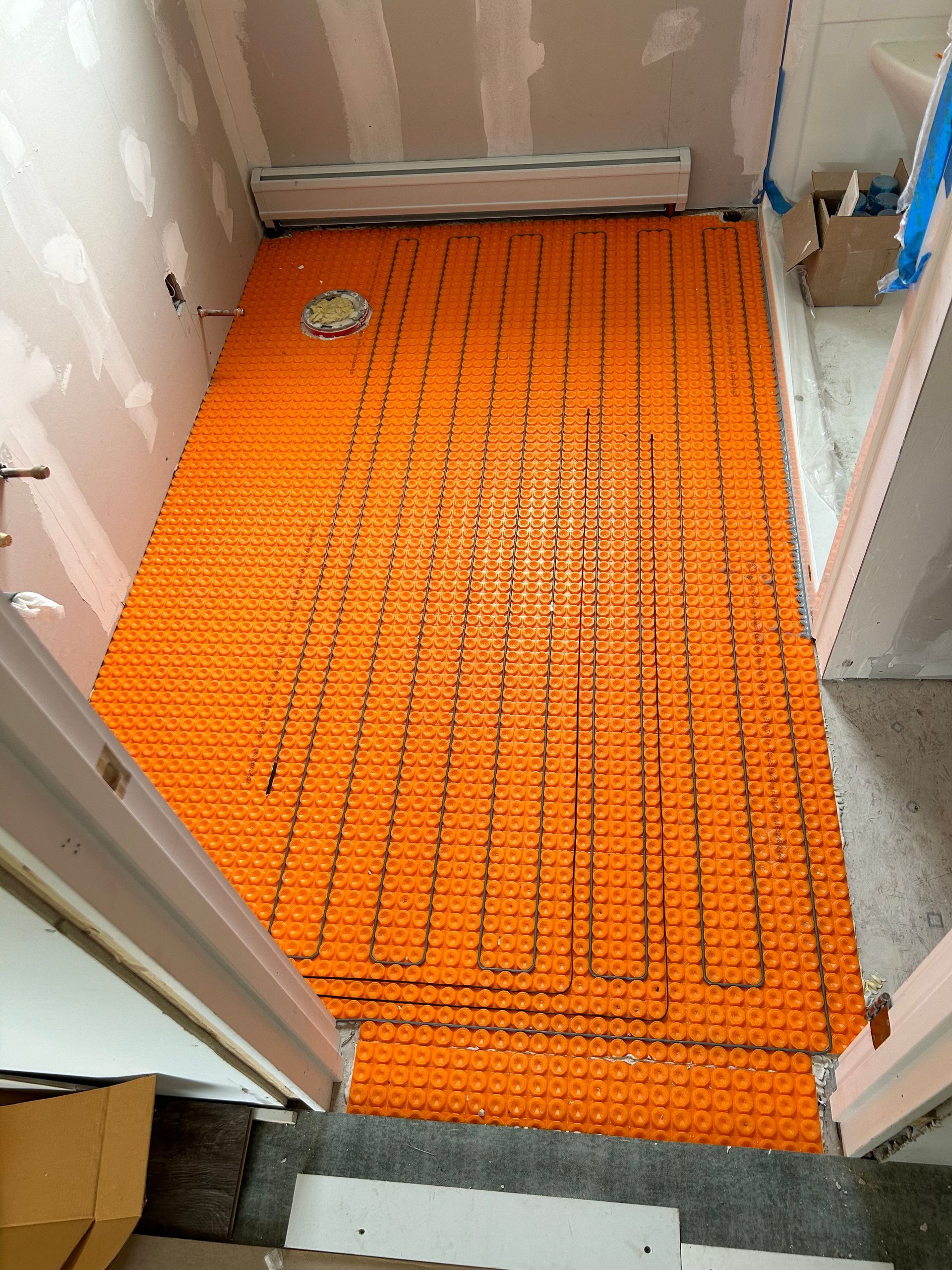 Orange underlayment covering a small bathroom floor under renovation, with a drain visible near the back.