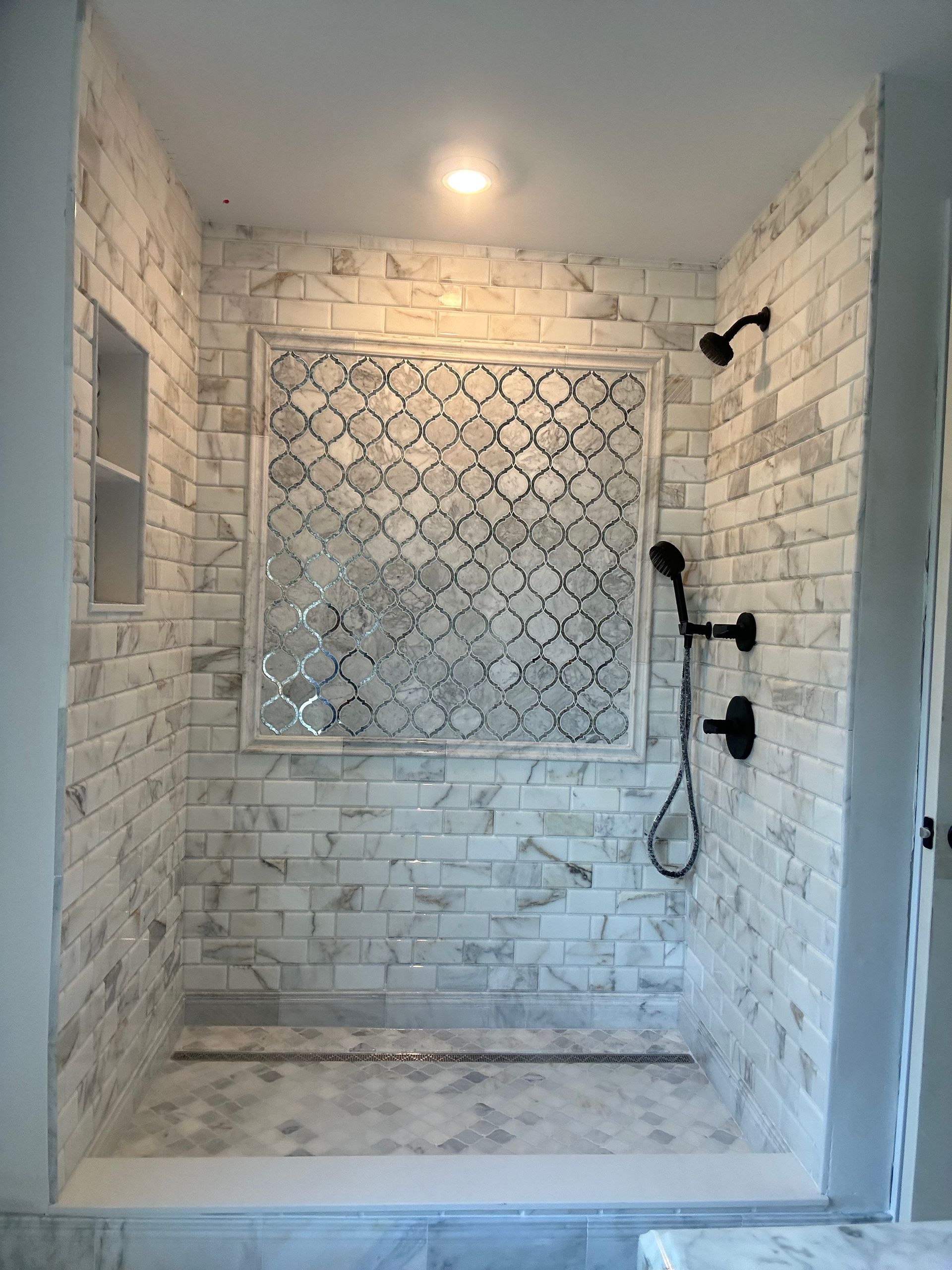 Empty tiled walk-in shower with mosaic accent wall and black fixtures.