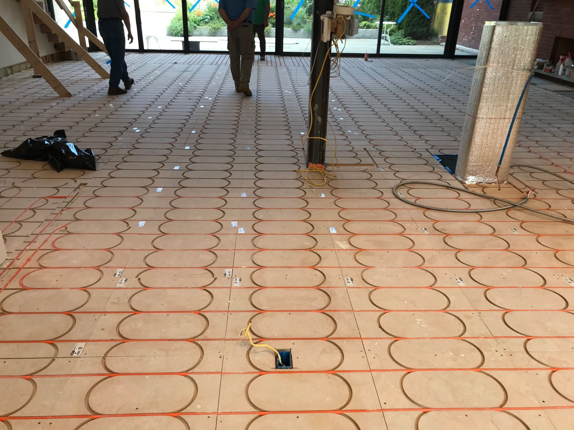 Covered walkway with patterned tile floor, concrete pillars, and a few people’s legs in the background.