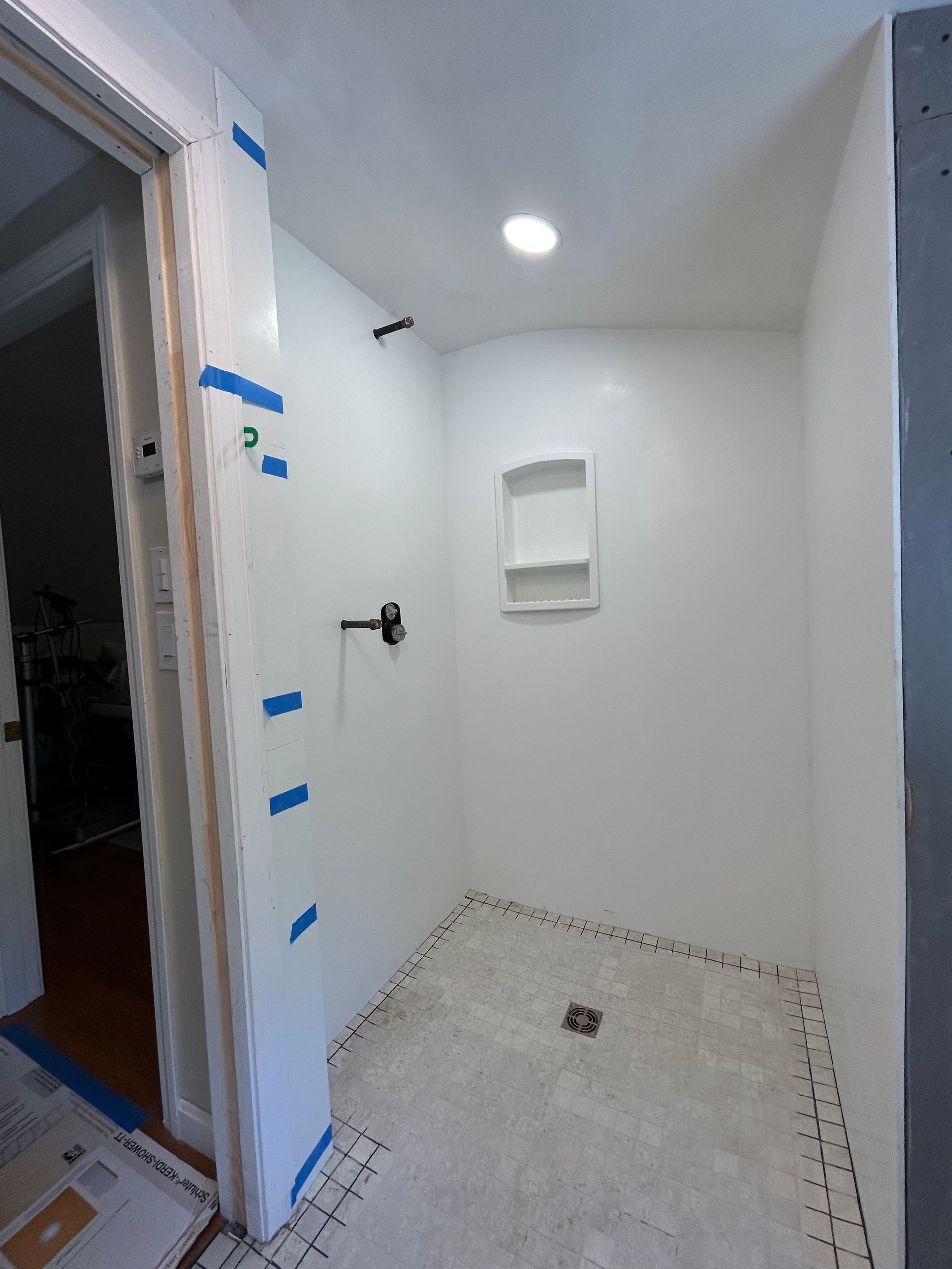 Small white-tiled shower room with built-in shelf, wall shower fixture, and floor drain.