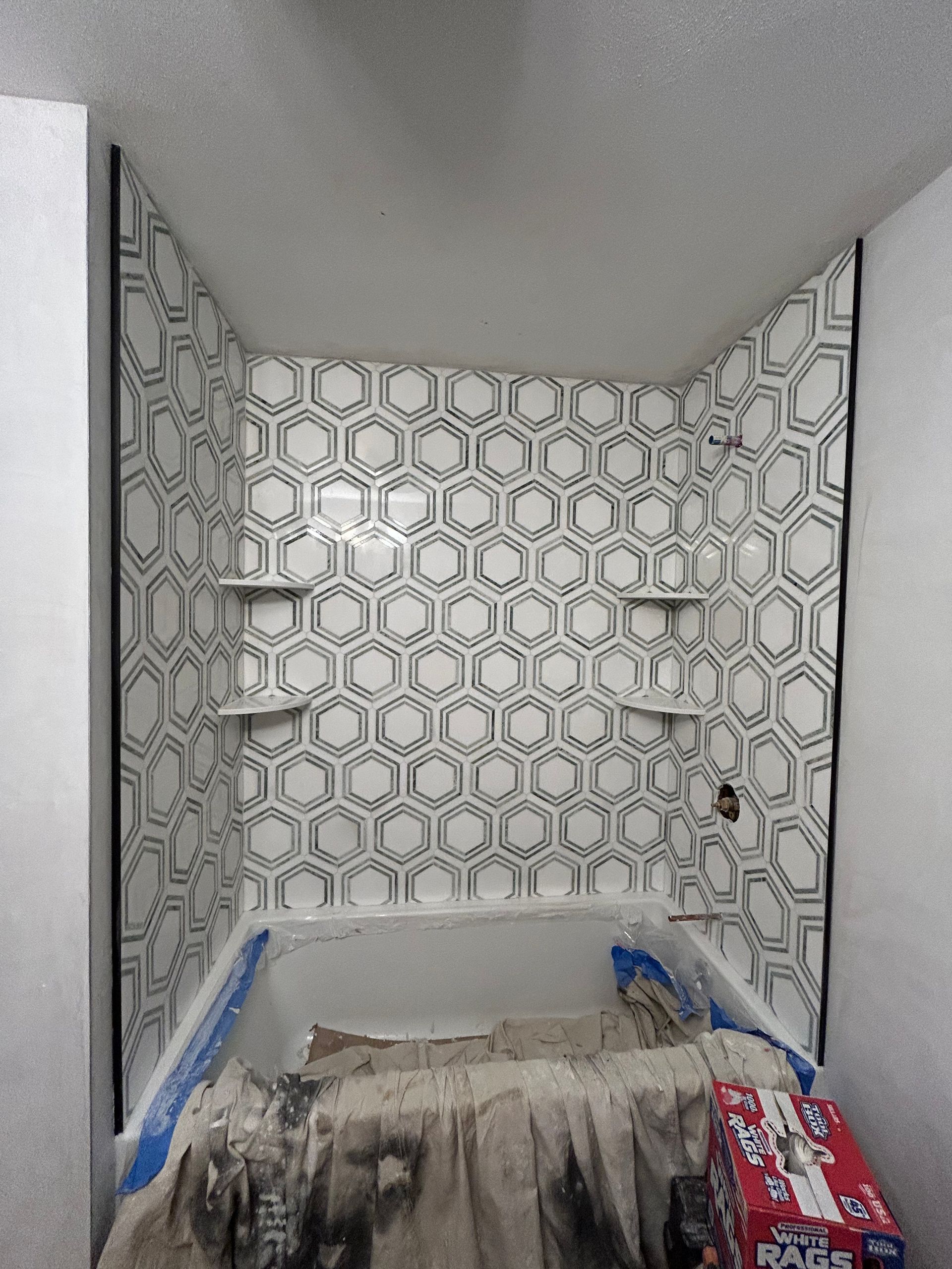Bathroom shower under renovation with geometric tile walls and a tub covered in plastic and debris