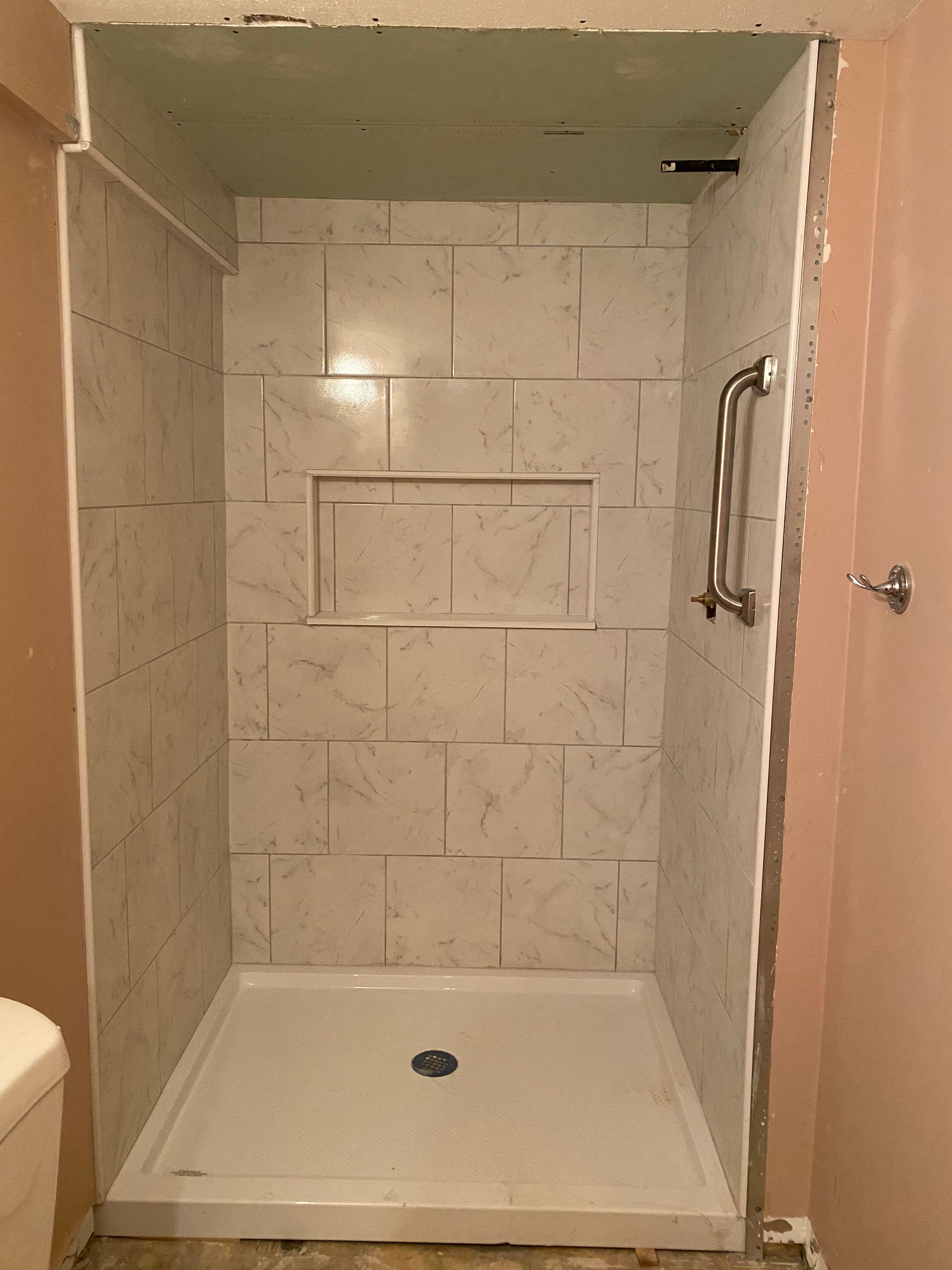 Empty tiled shower with built-in shelf, grab bar, and white shower base in a bathroom.