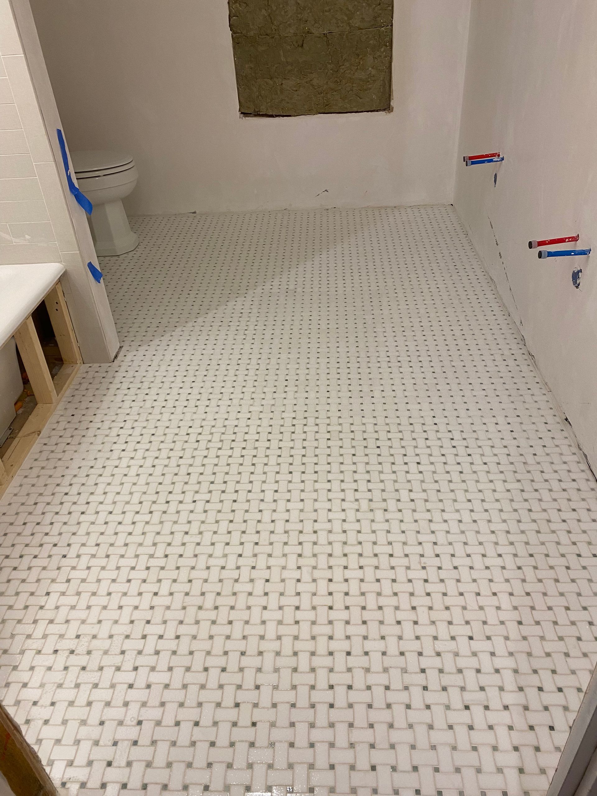 Empty bathroom with tiled floor, a tub on the left, and a covered window at the back.