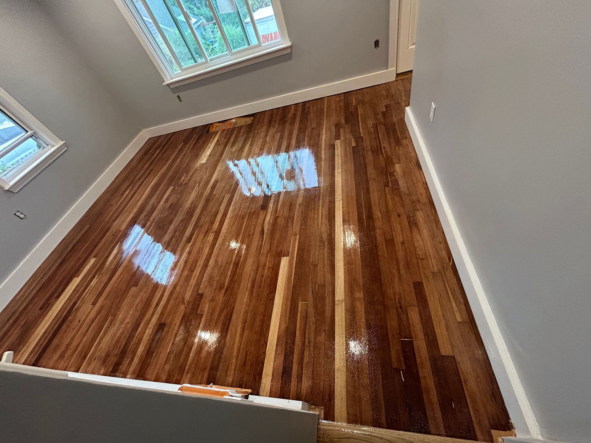 Empty room with glossy hardwood floors and two windows letting in daylight