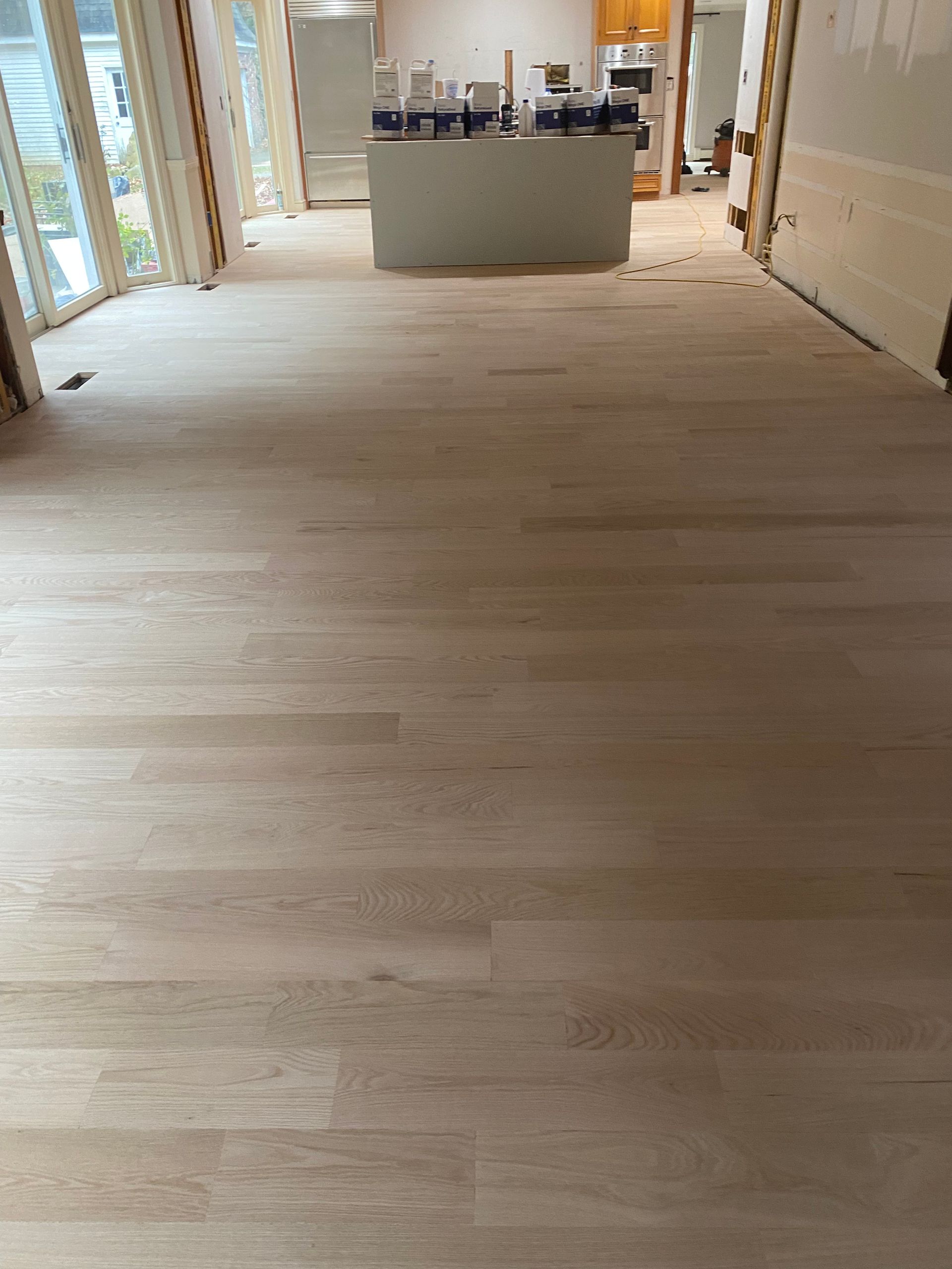 Renovated room with light wood flooring and a kitchen island in the background