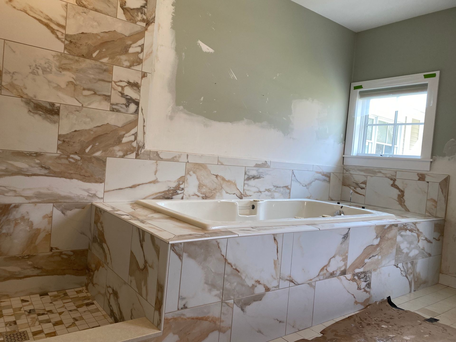 Marble-tiled bathroom with a built-in soaking tub and unfinished walls, lit by a window