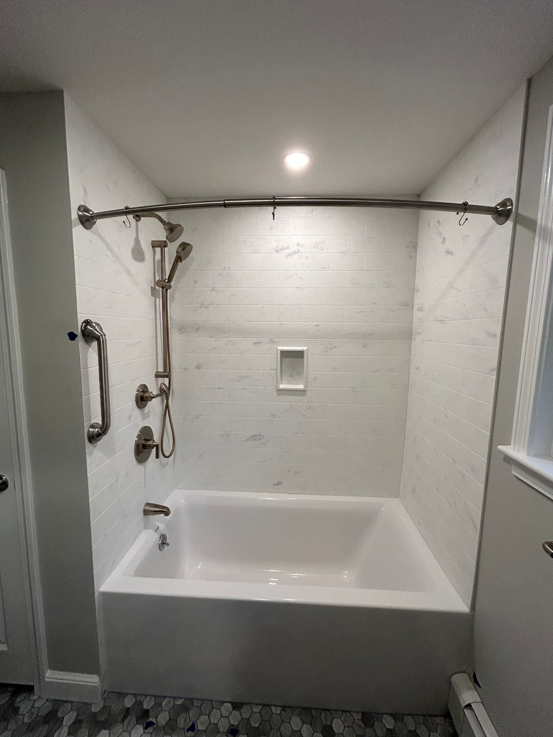 Bathroom with white bathtub, shower curtain rod, handheld shower, and grab bars in a tiled alcove.
