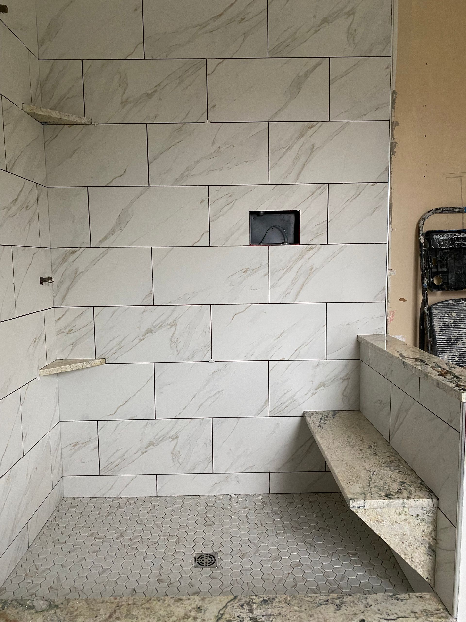 Partially tiled bathroom wall with a small wall opening and a built-in bench under construction