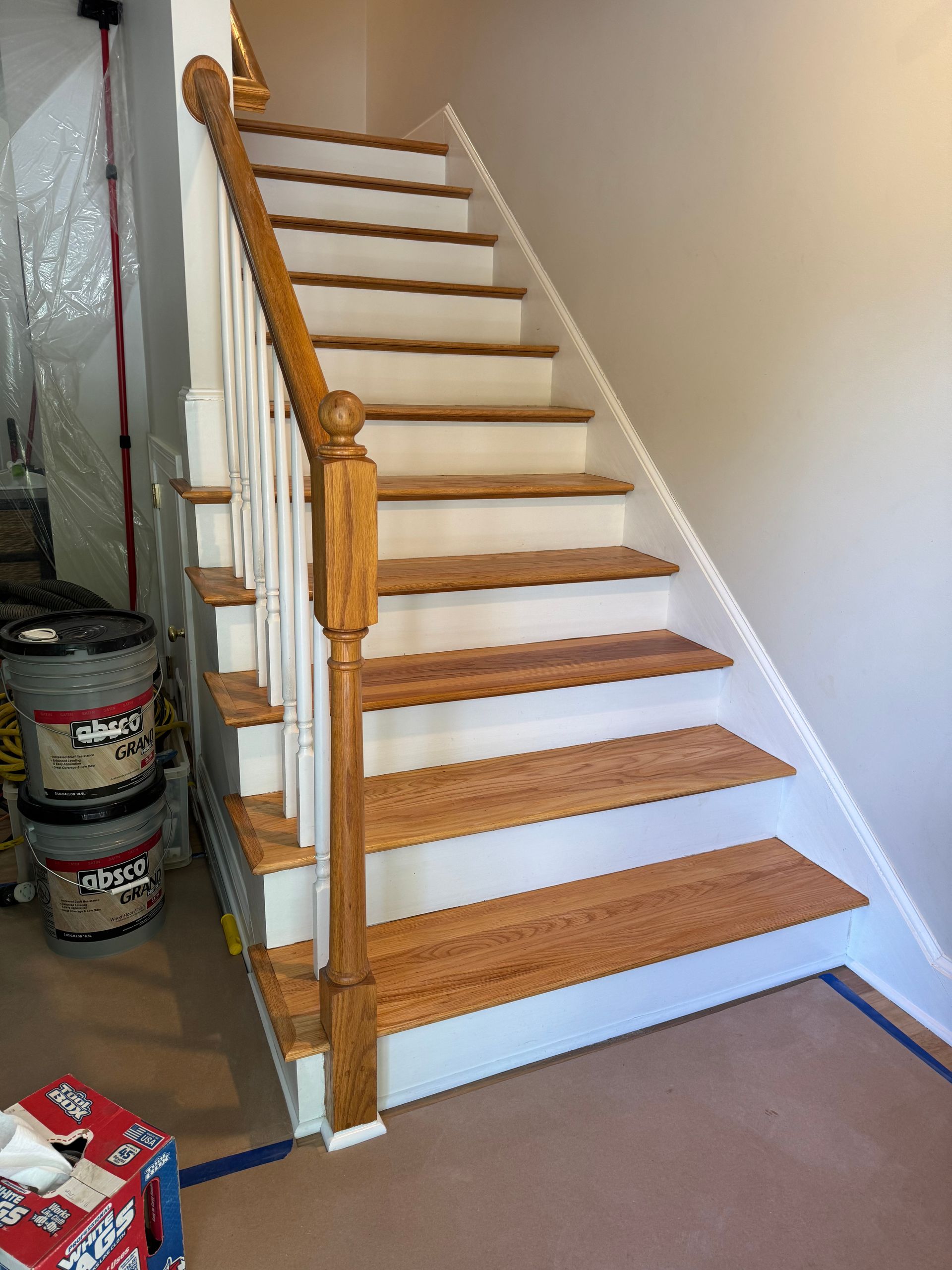Wooden staircase with white carpeted steps and a banister in an unfinished indoor space.